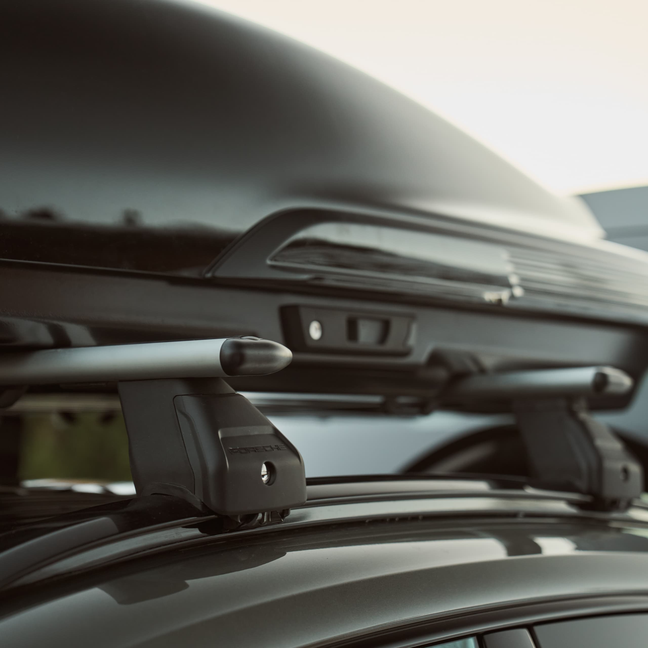 Toit de voiture avec coffre de toit noir et barres transversales argentées, vue rapprochée, mettant en avant le design élégant et les détails de fixation.