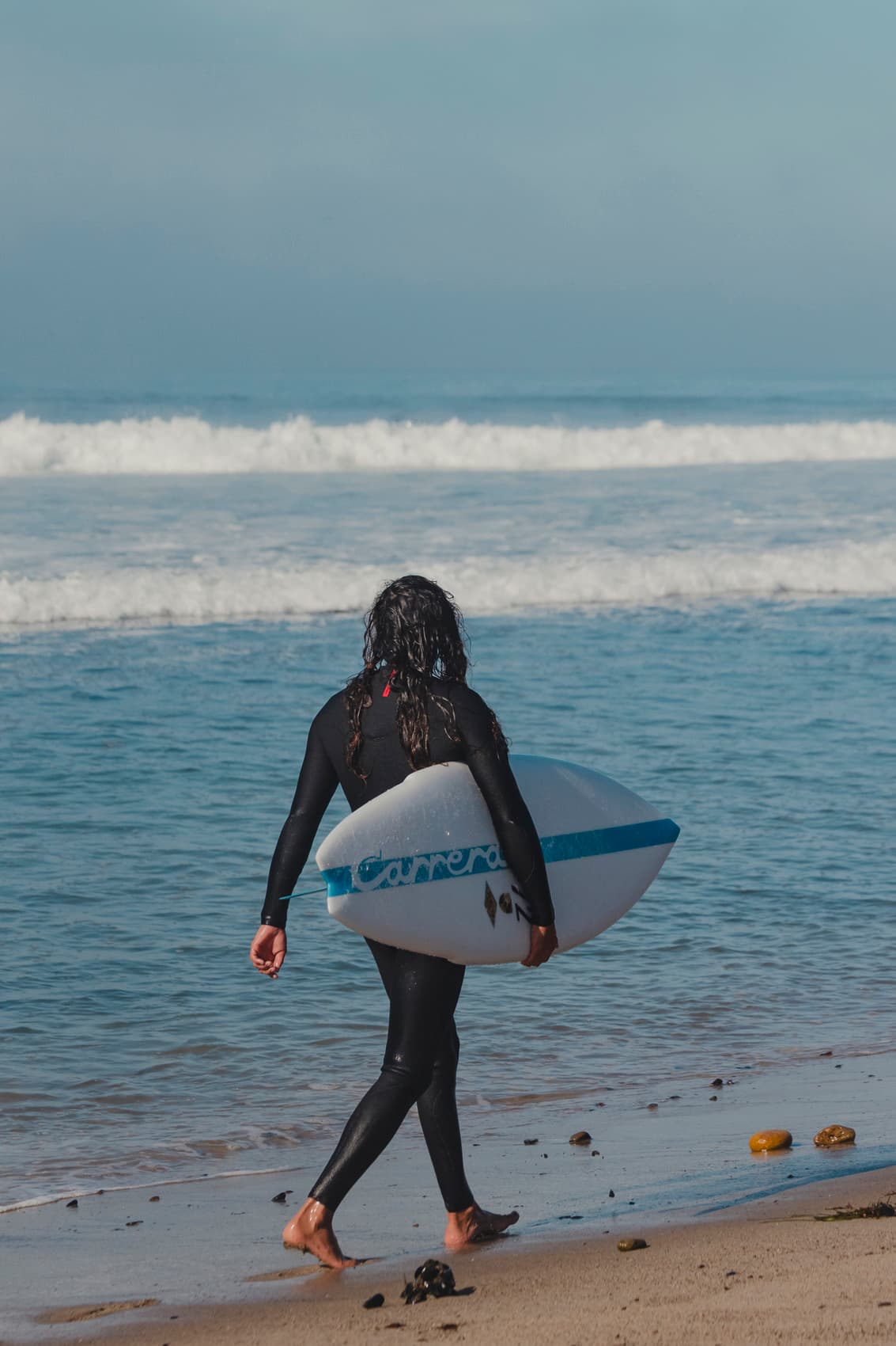Man standing on beach holding a white Porsche Surfboard with blue Stipe