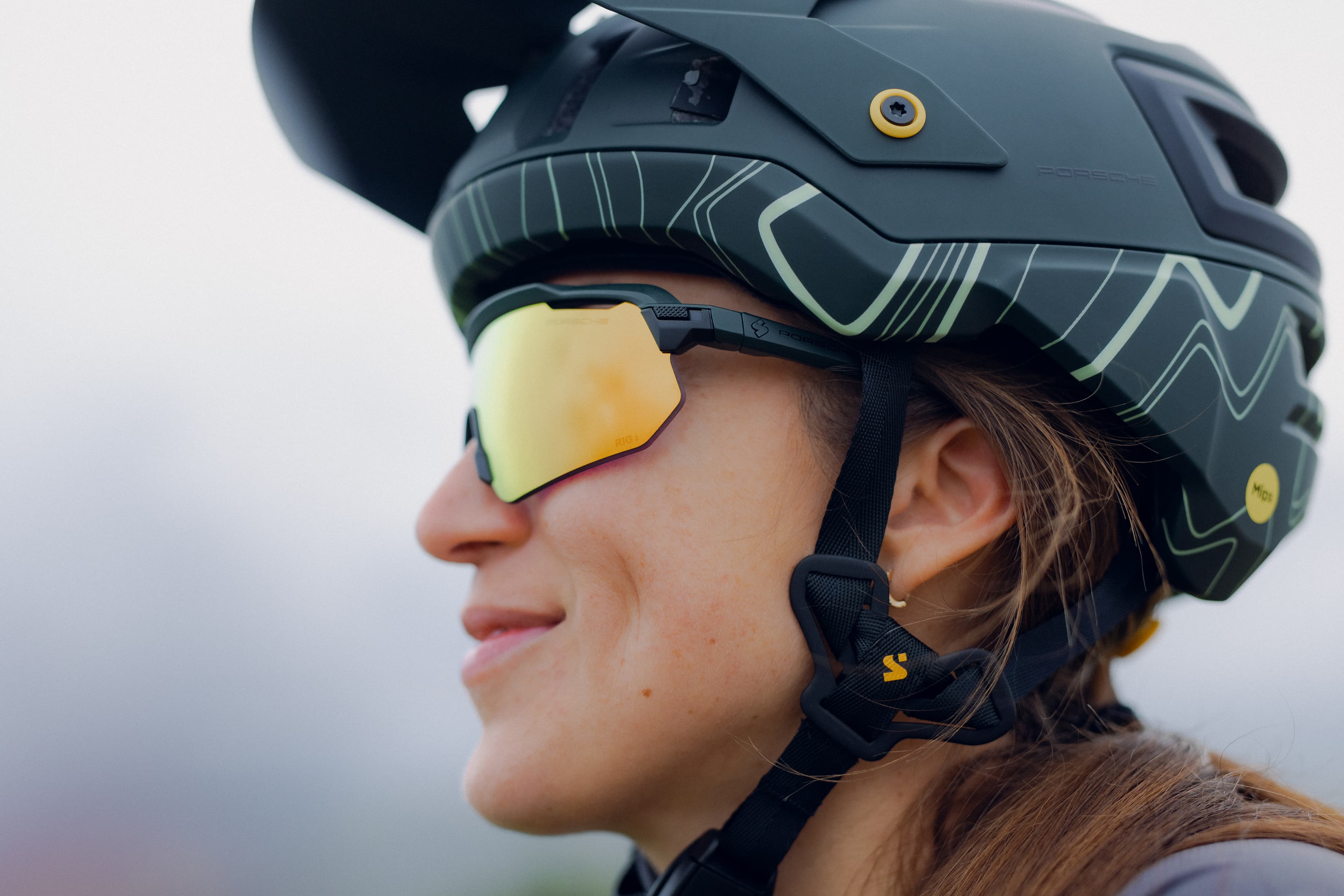 Side view: Person wearing a black bicycle helmet with a line pattern and gold mirrored sports glasses.