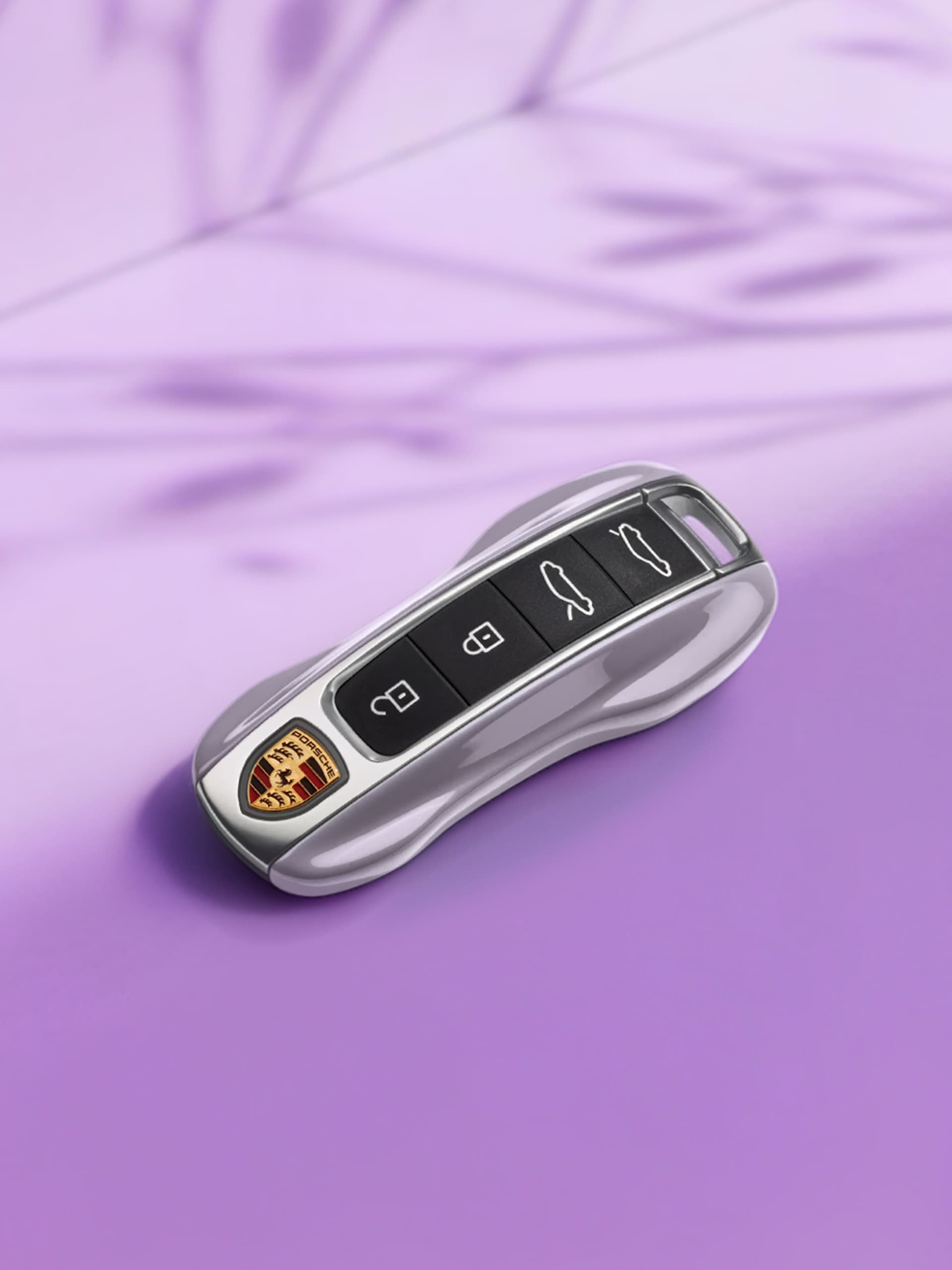Chave de carro Porsche prateada com botões pretos, sobre fundo roxo.