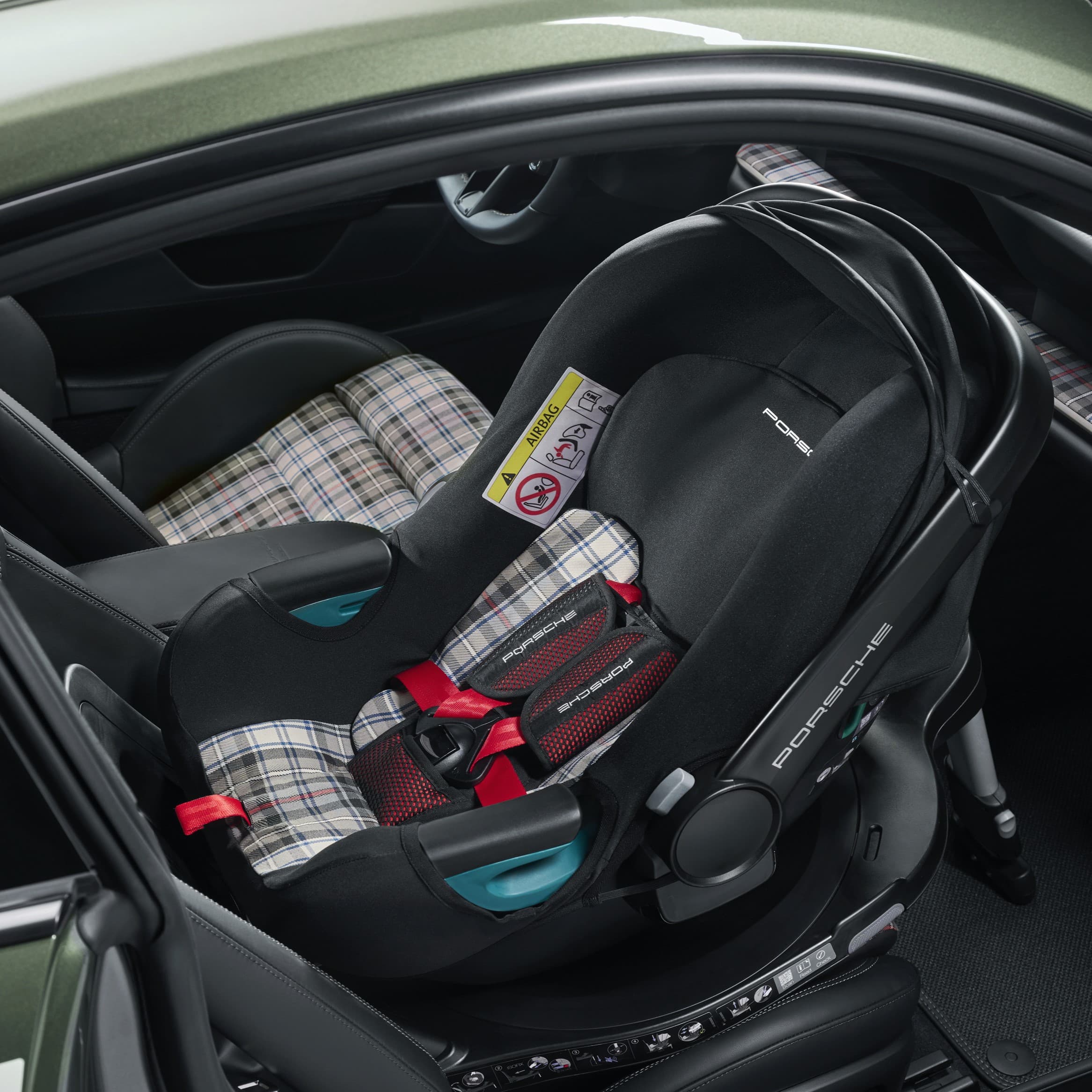 Schwarzer Porsche-Kindersitz mit rotem Gurt und kariertem Polster, auf dem Rücksitz eines Autos installiert.