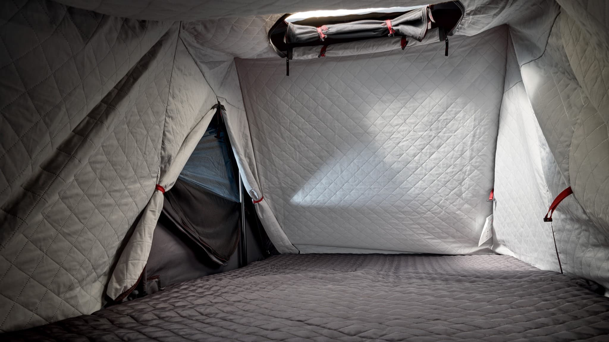 Quilted interior of a gray tent with red straps, featuring a window and a soft floor, creating a cozy camping space.