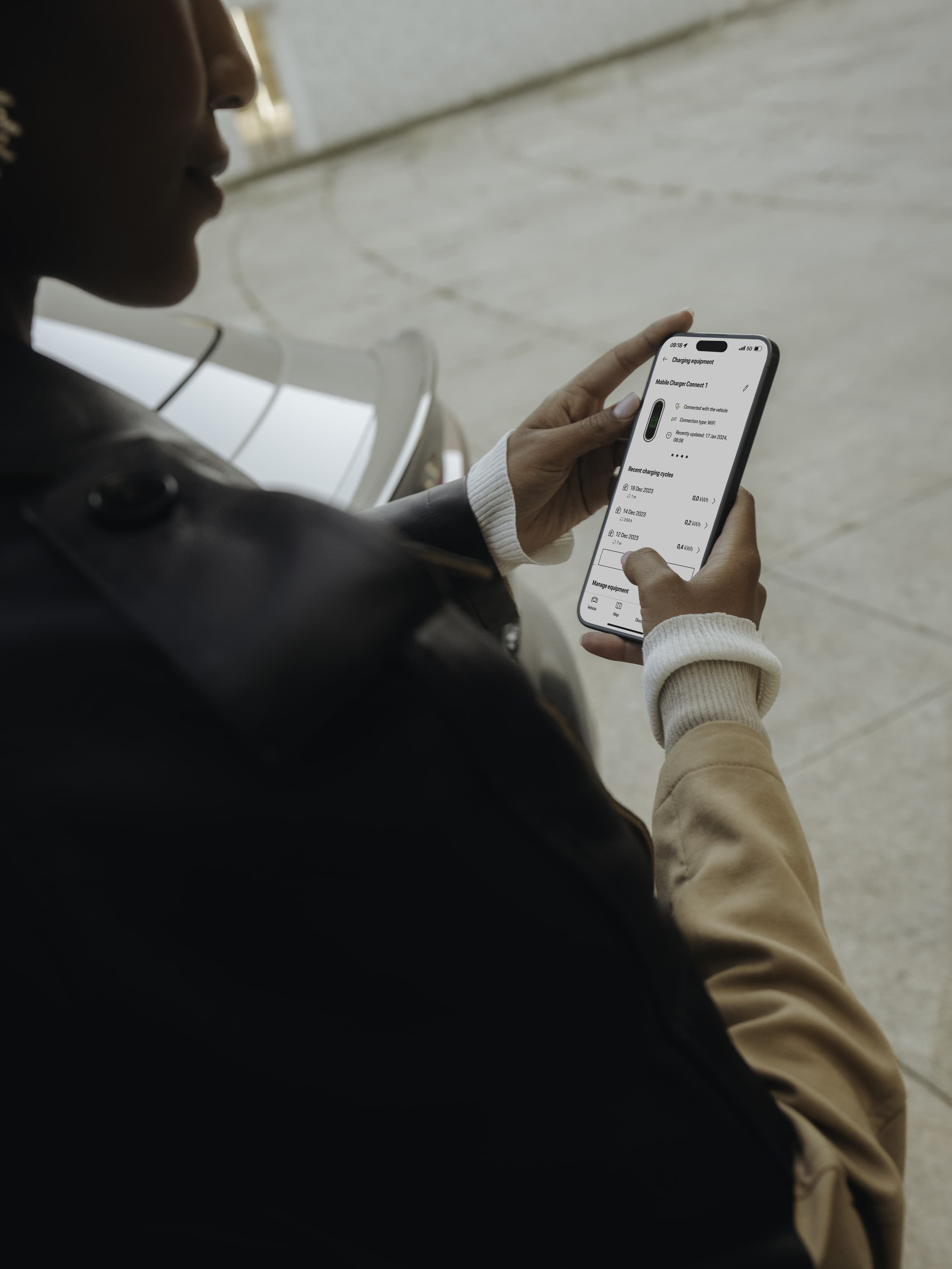 Person in einer Jacke, die eine Smartphone-App in der Nähe eines geparkten Autos verwendet, zeigt Ladeinformationen auf dem Bildschirm an.