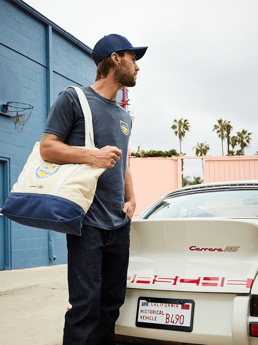 Man standing next to Porsche 911 with a beach bag on his shoulder