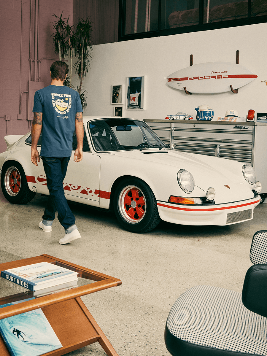 Man walking in Garage with Porsche 911 and Surfboard on the wall