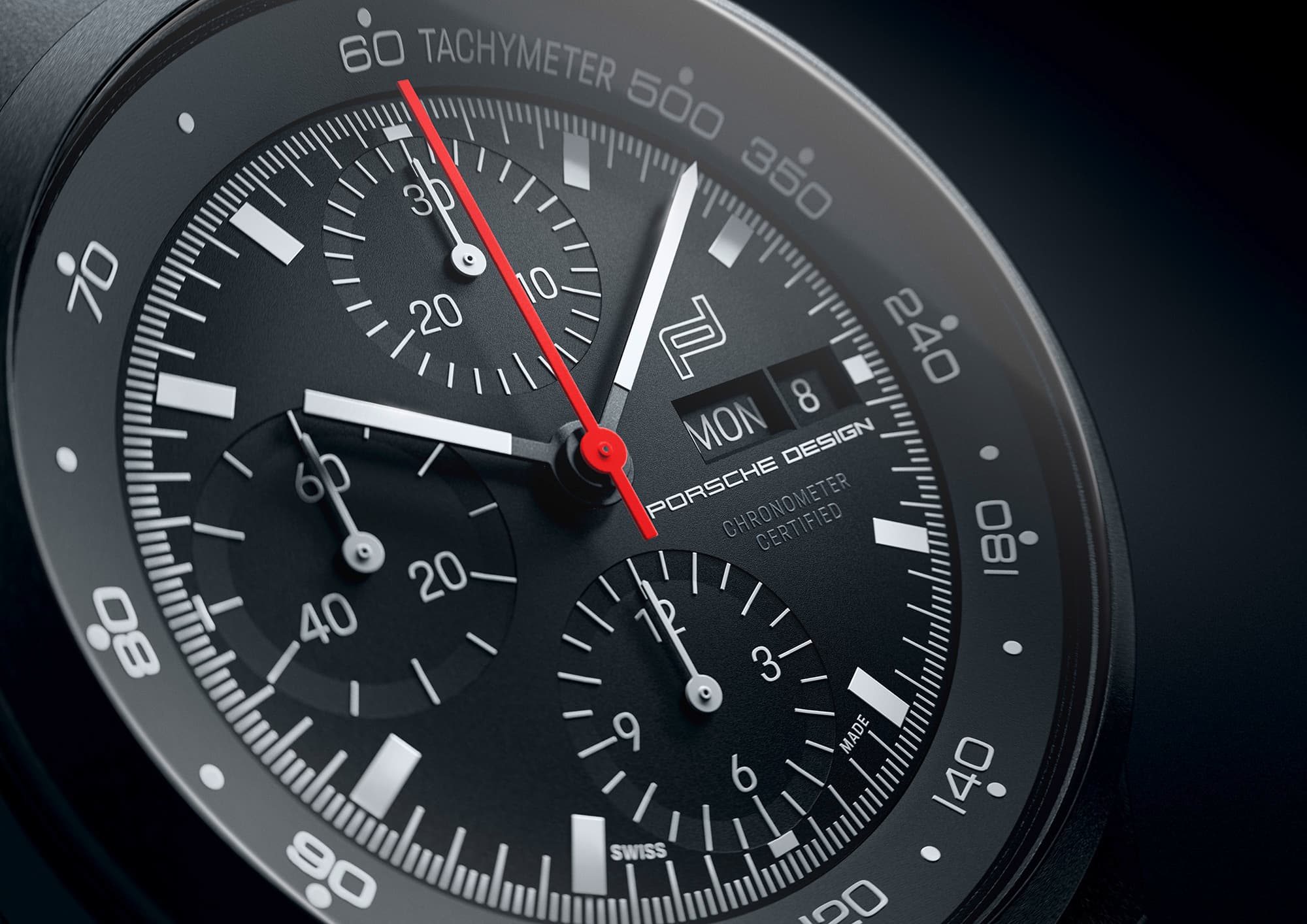 Close-up of a black Porsche Design chronograph with a red second hand and tachymeter scale.