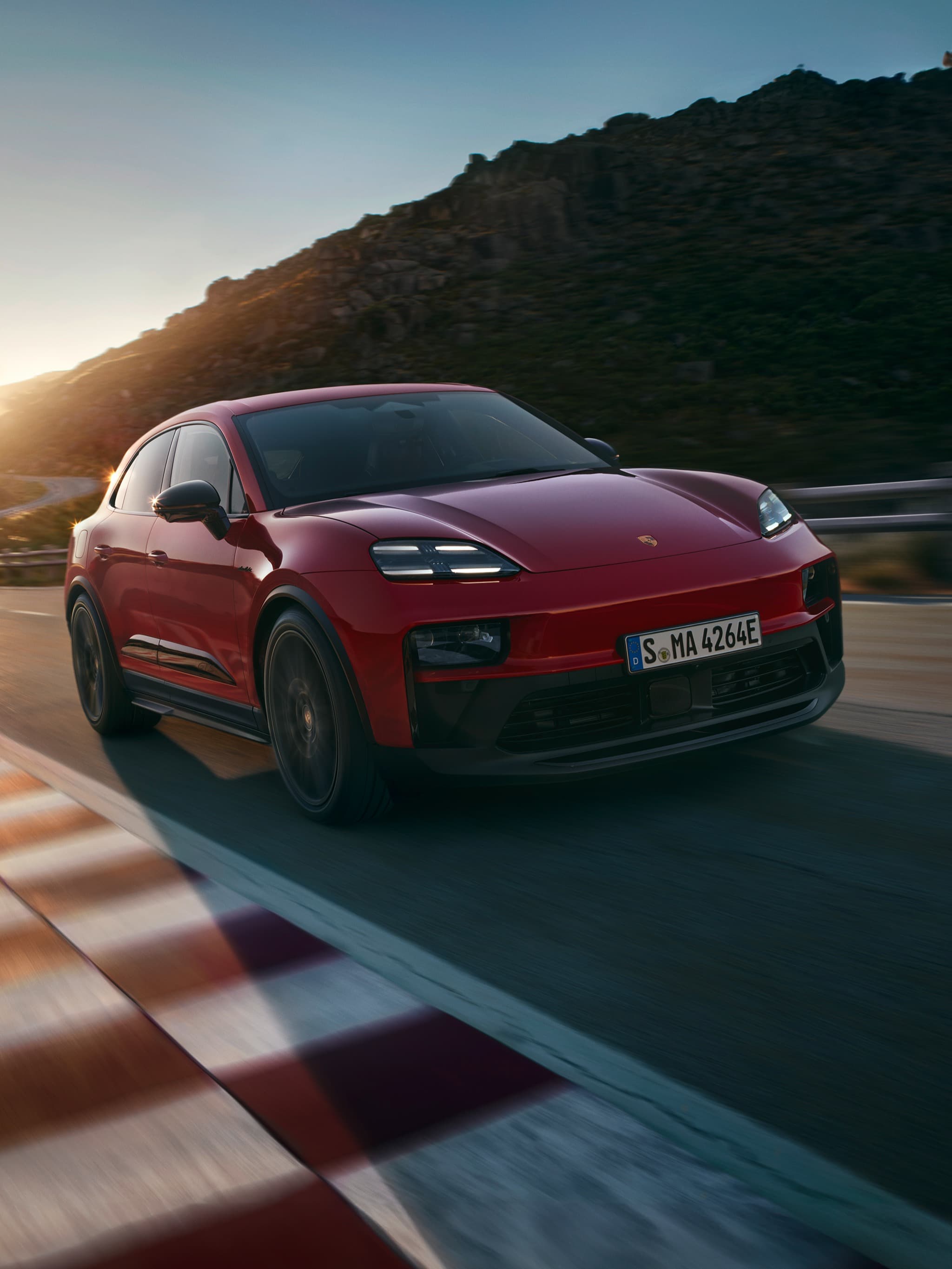 Roter Porsche Macan fährt bei Sonnenuntergang auf kurviger Bergstraße, Frontansicht mit Motion Blur.