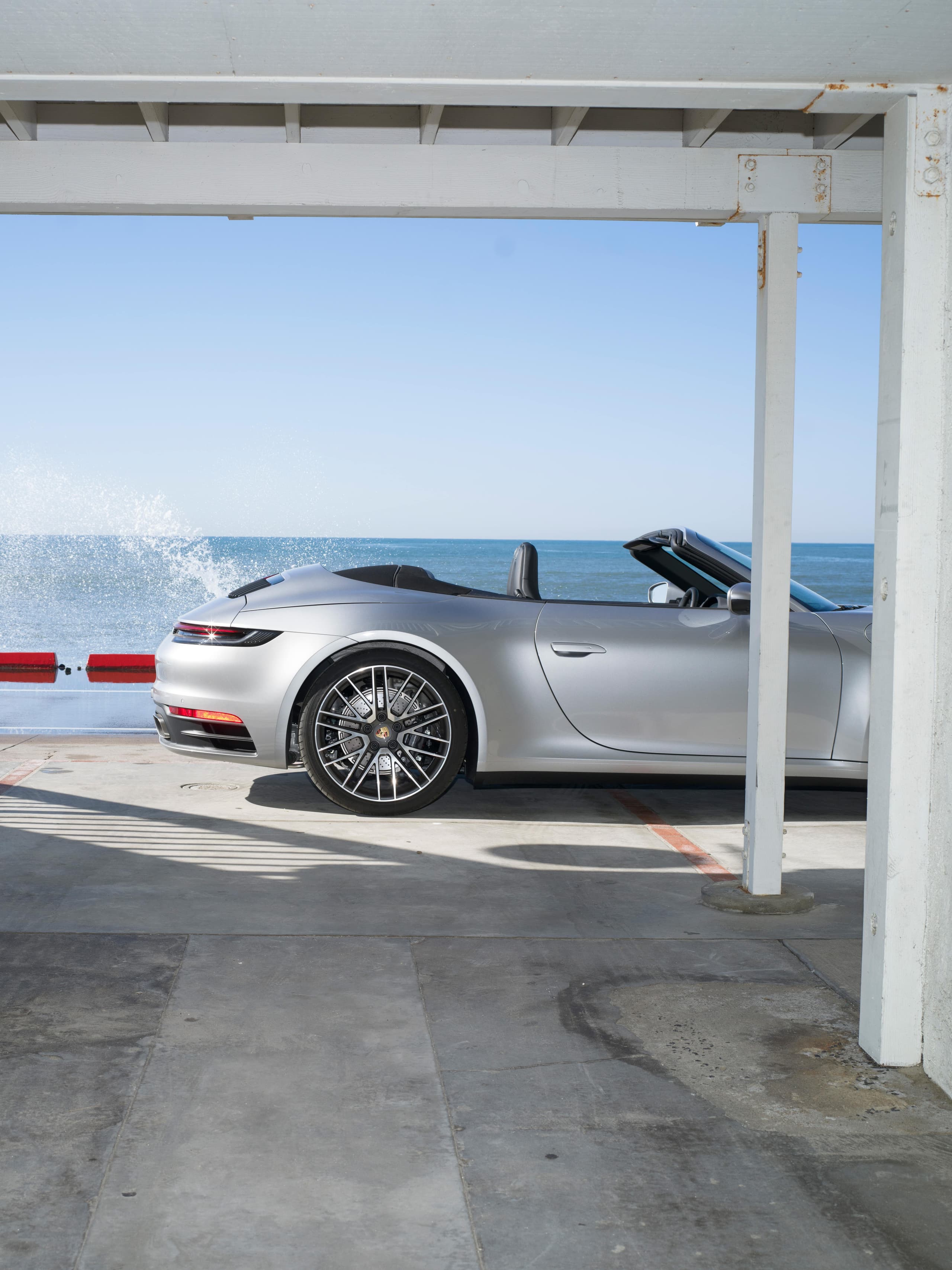 Pictured is the a silver Porsche 911 from the side. Though only the rear part is visible. In the background is the water.