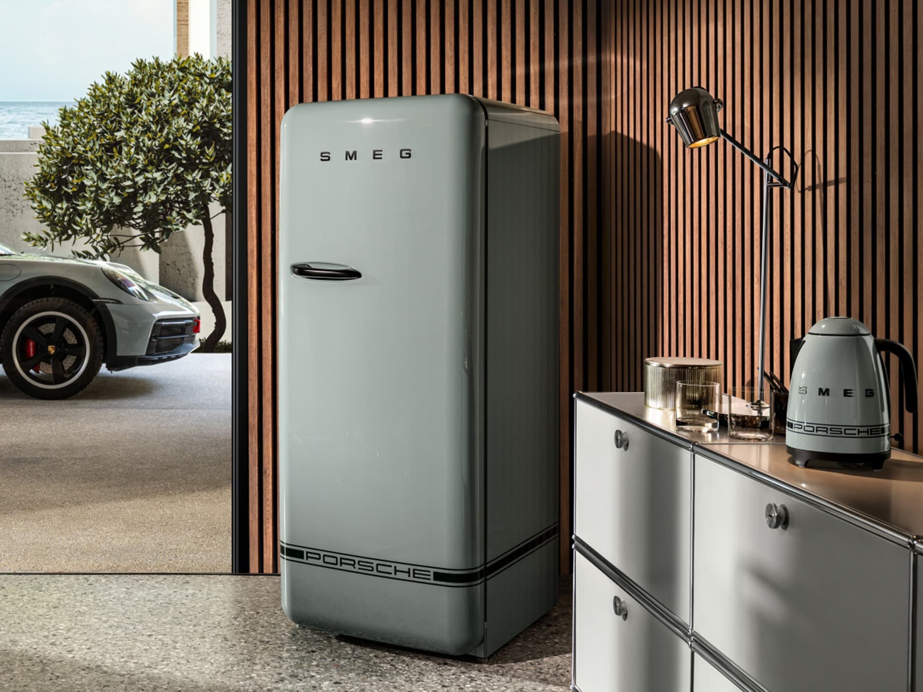 Retro-style grey fridge and kettle with Porsche branding, set against a wooden slat wall and modern decor.