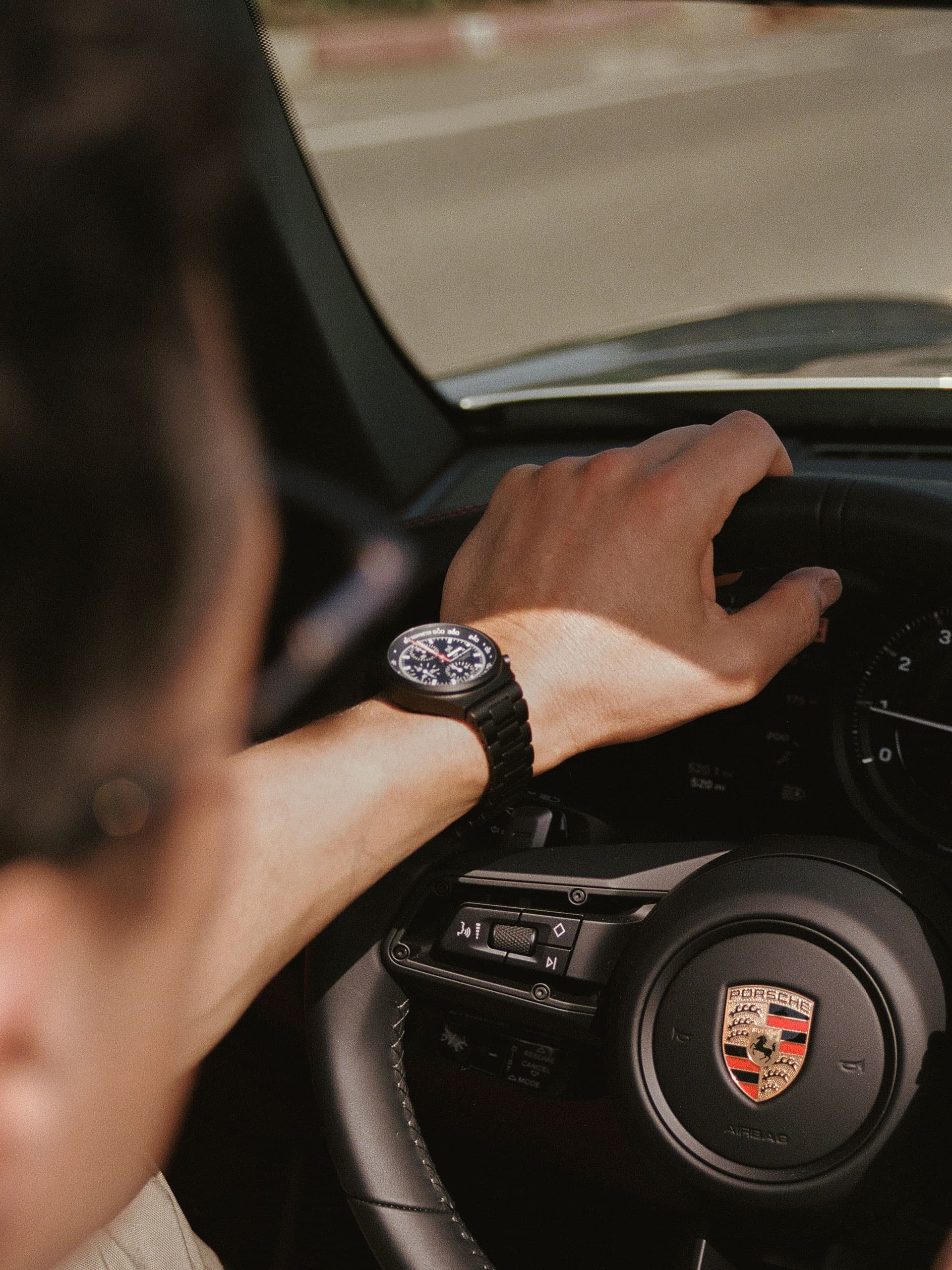 You can see a person sits behind the wheel of a Porsche car and you can see a Porsche Design watch on the wrist