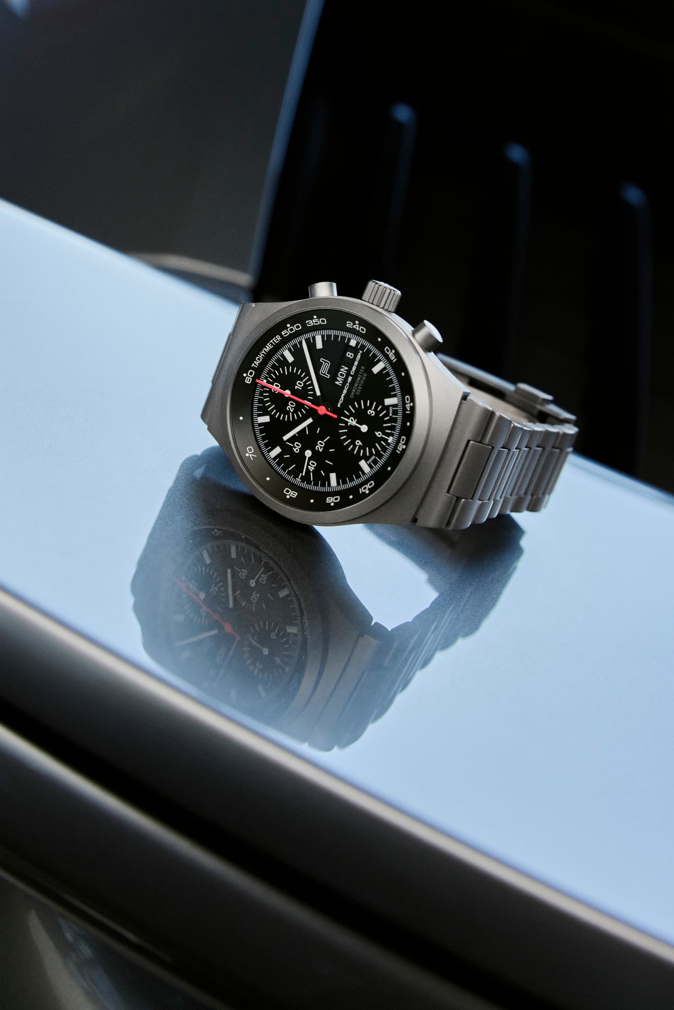Silver chronograph wristwatch with black dial and red seconds hand, on a glossy surface.
