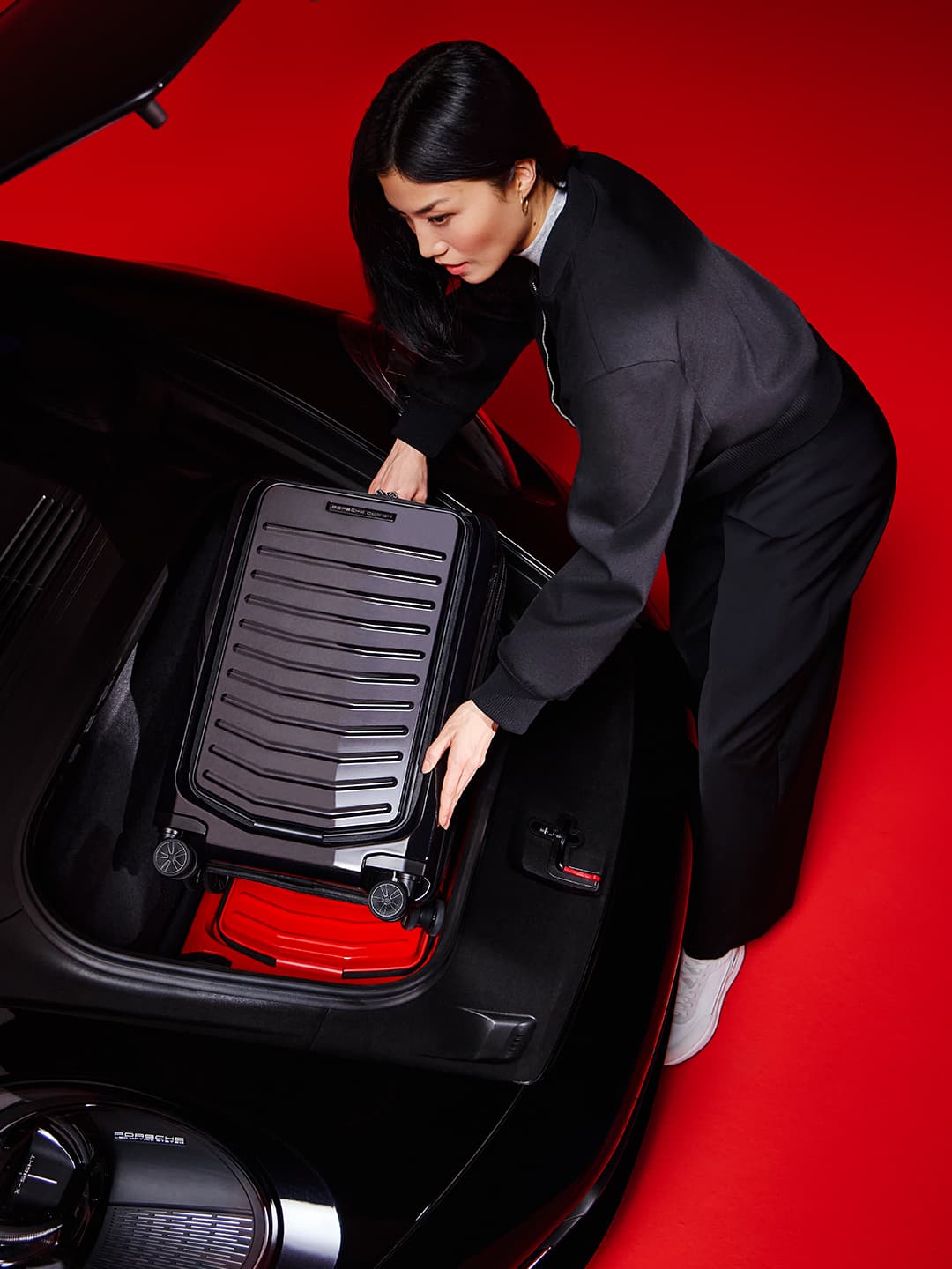 Woman putting a black Porsche Design suitcase into a car