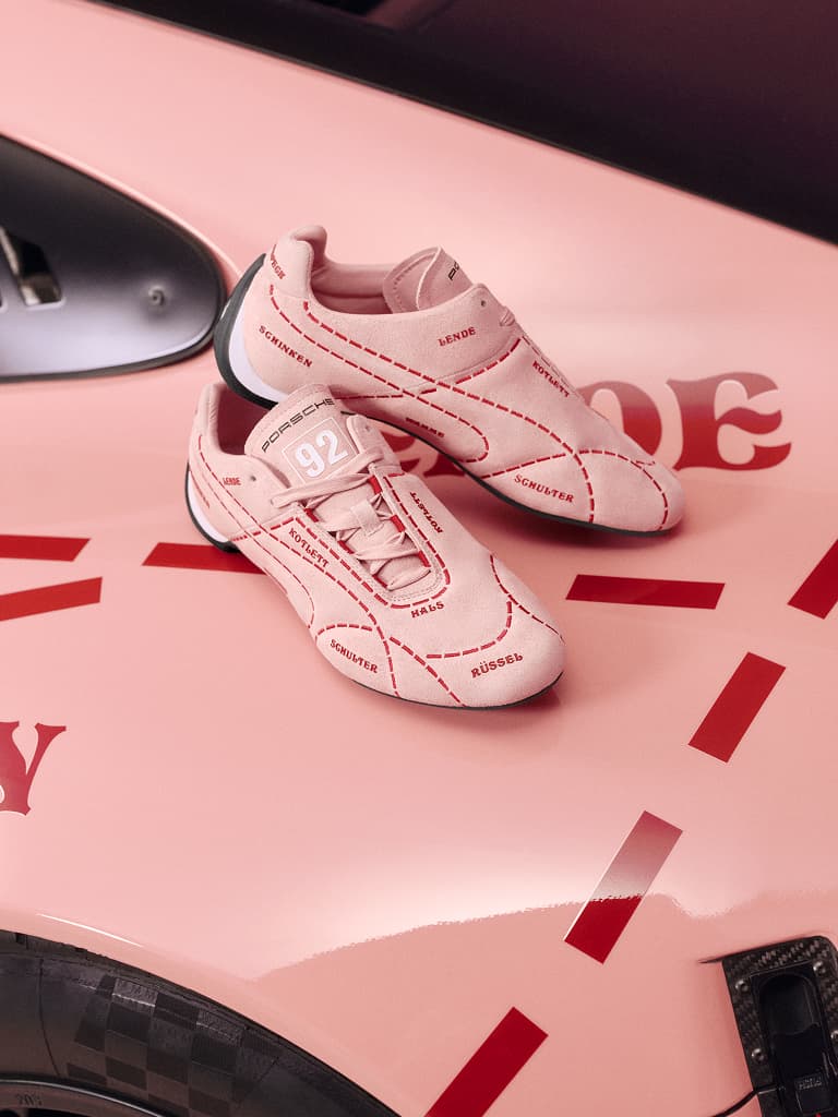Zapatillas rosas con costuras rojas y texto, colocadas sobre el capó de un coche rosa a juego con detalles rojos.