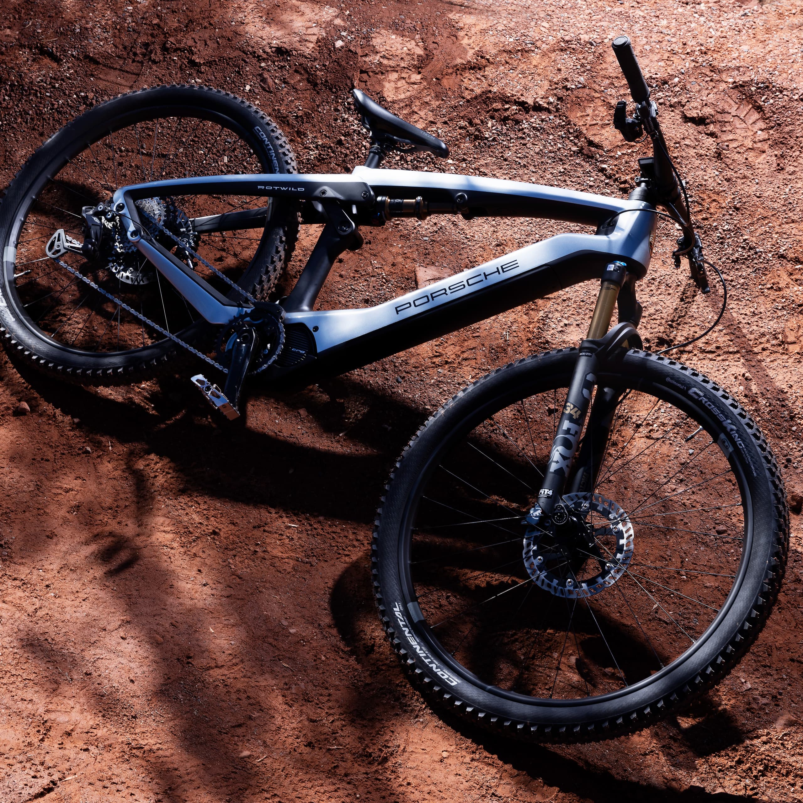 Sleek black and silver Porsche mountain bike on a sunlit, reddish-brown dirt path.
