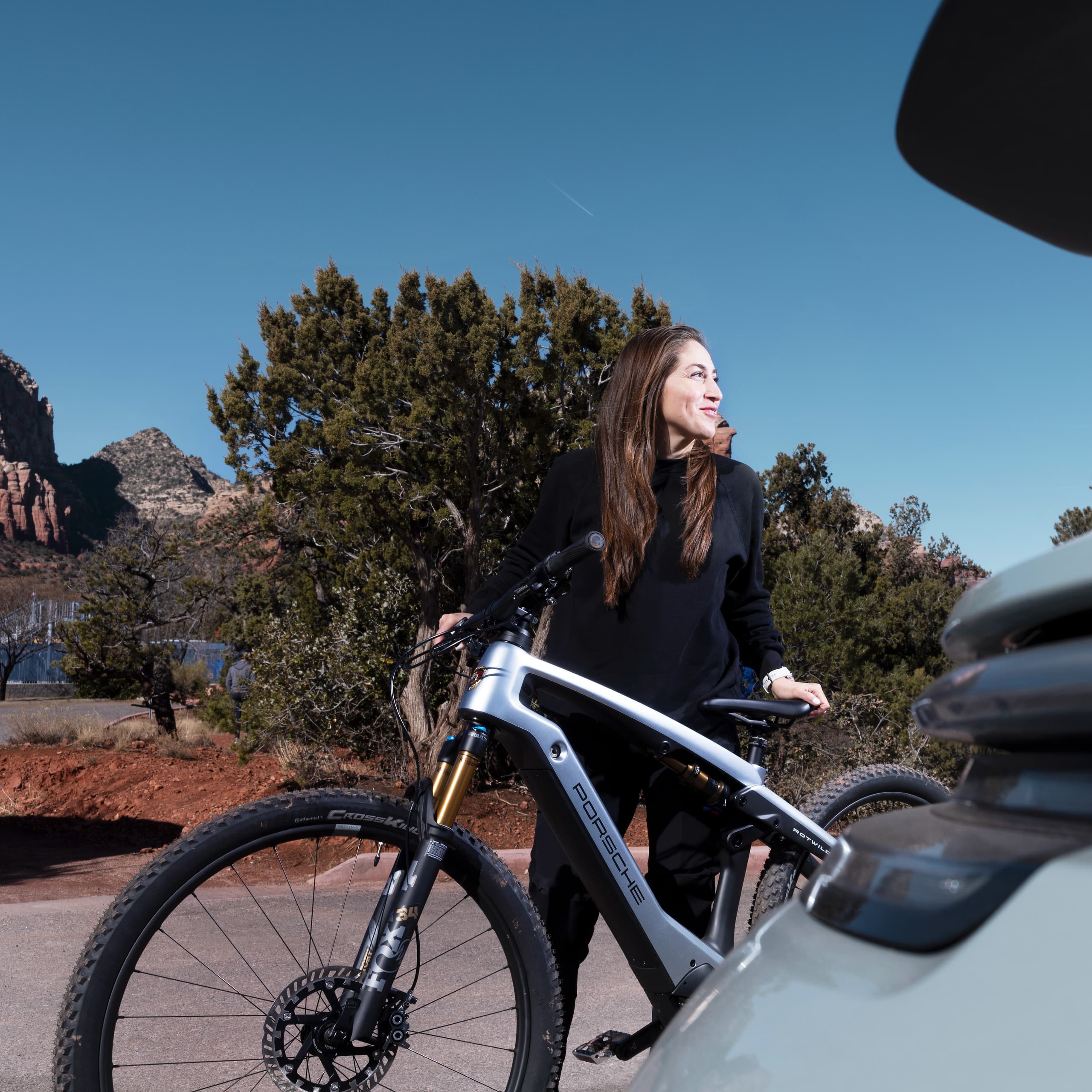 You can see a woman with her Porsche eBike, small trees and blue sky