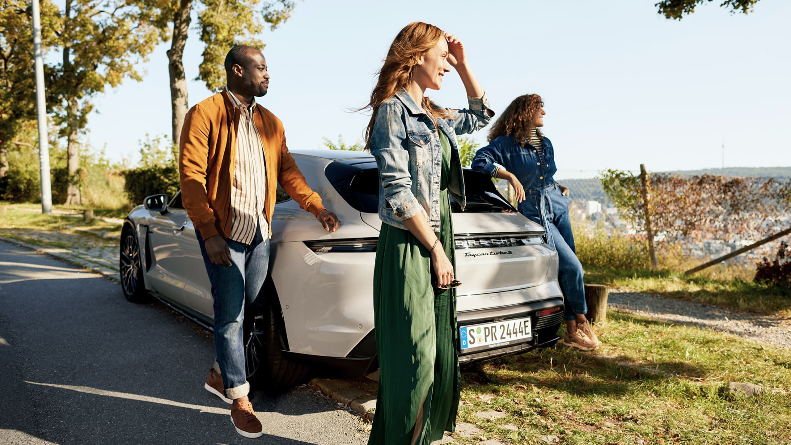 You can see tree people around a grey Porsche Taycan on the grass