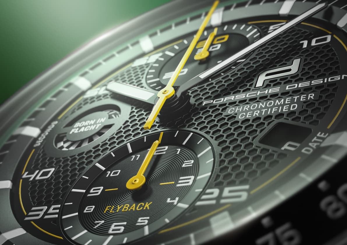 Close-up of a Porsche Design chronograph dial in black with a honeycomb pattern and yellow hands.