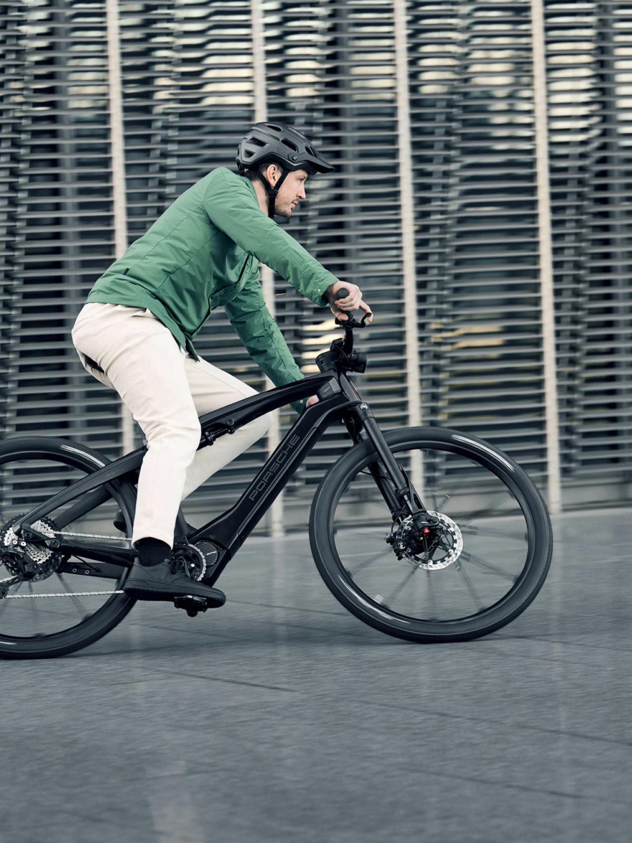 Pictured is a cyclist with a green jacket from the side riding a Porsche Ebike Sport.