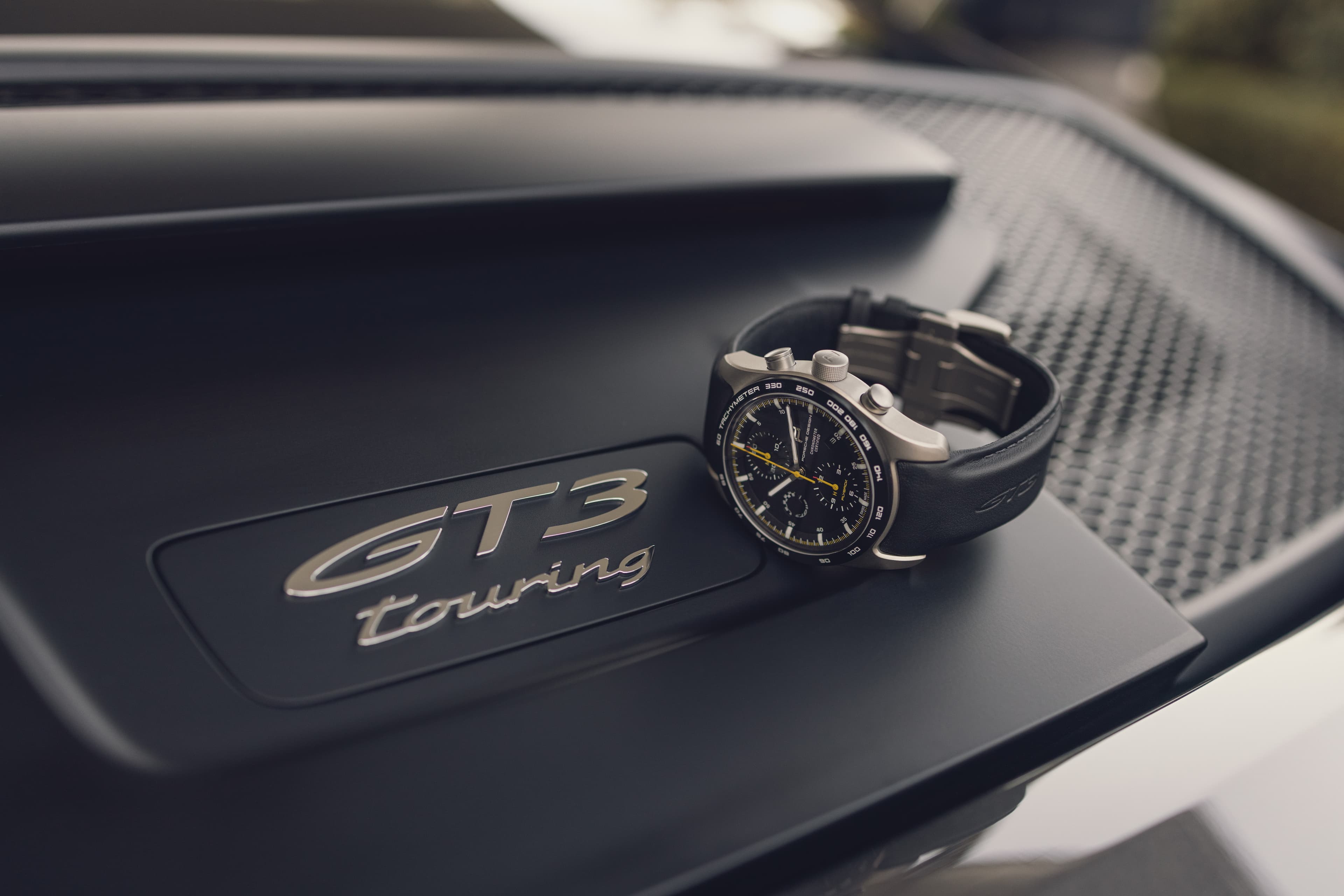 Chronograph watch with black leather strap resting on a Porsche 911 GT3 Touring engine cover.