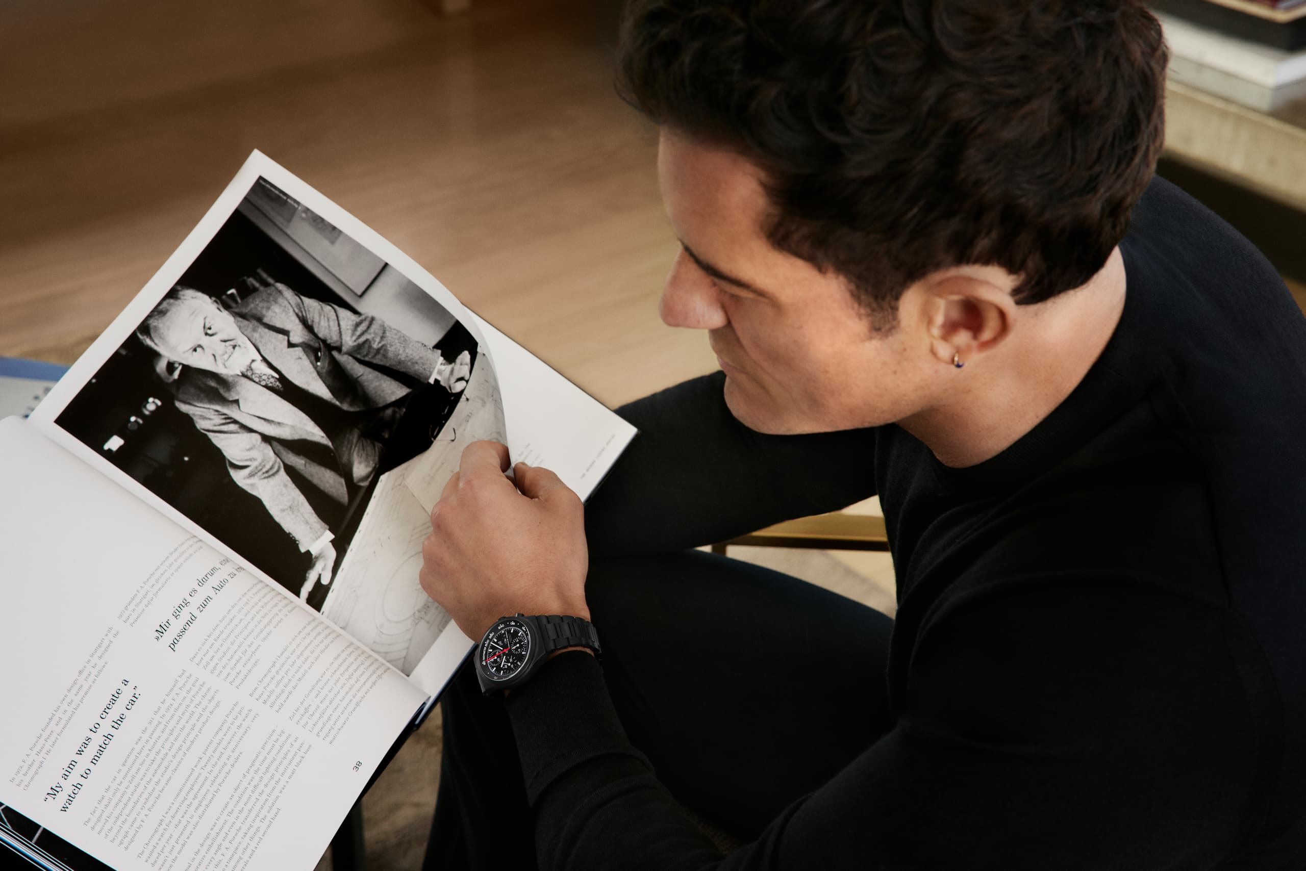 Orlando Bloom w zegarku Chronograph 1 – All Black Numbered Edition, czytający artykuł w magazynie o prof. Ferdinandu Alexandrze Porsche.
