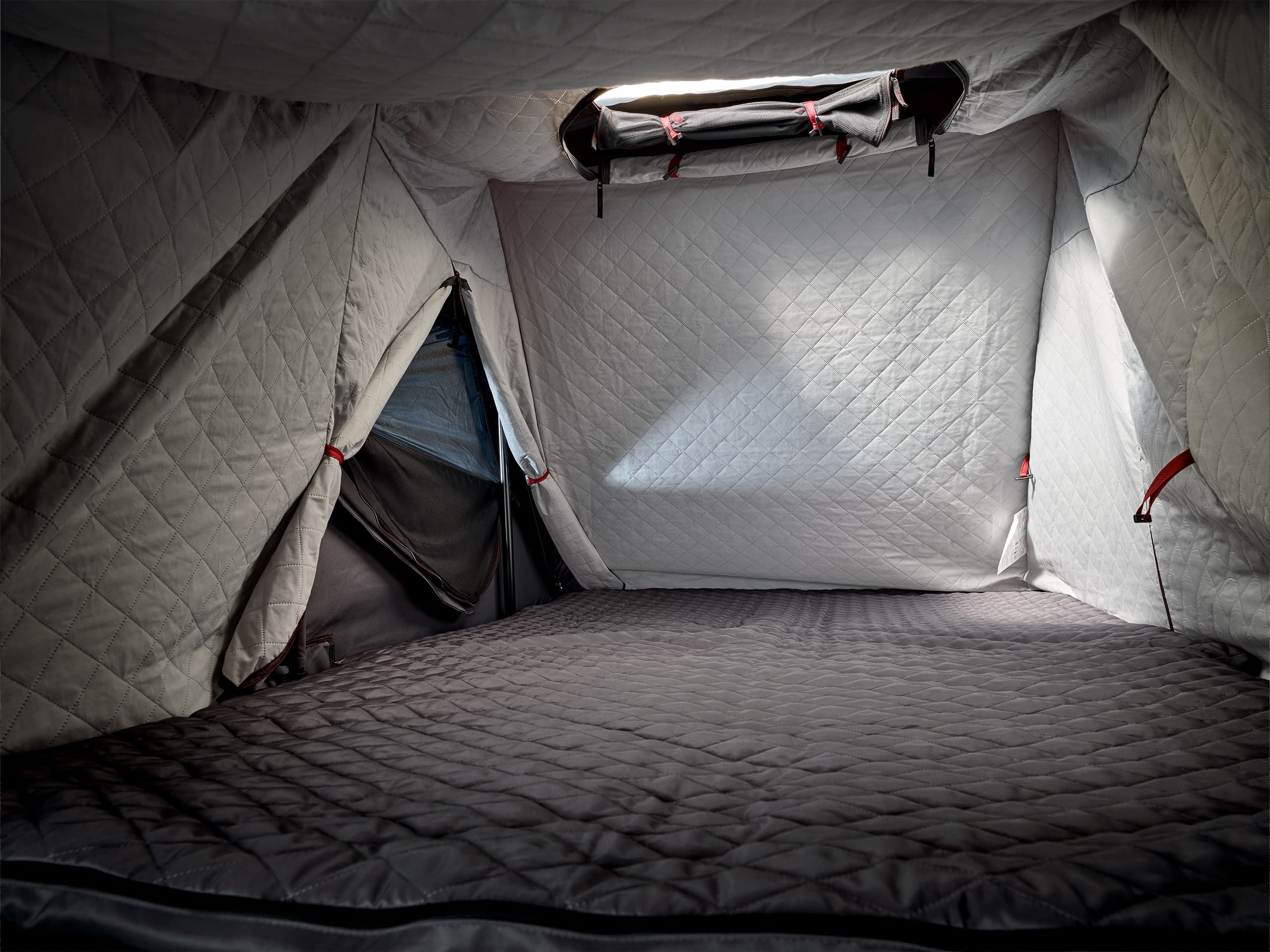 Quilted gray tent interior with a skylight, red accents, and a padded floor, creating a cozy and insulated space.