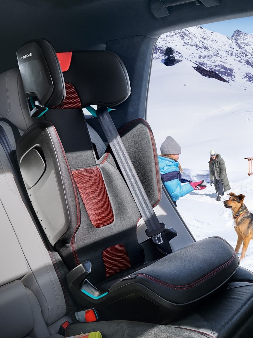 Car interior with child seat snowy mountain view outside. People and dog playing in snow wearing winter clothing