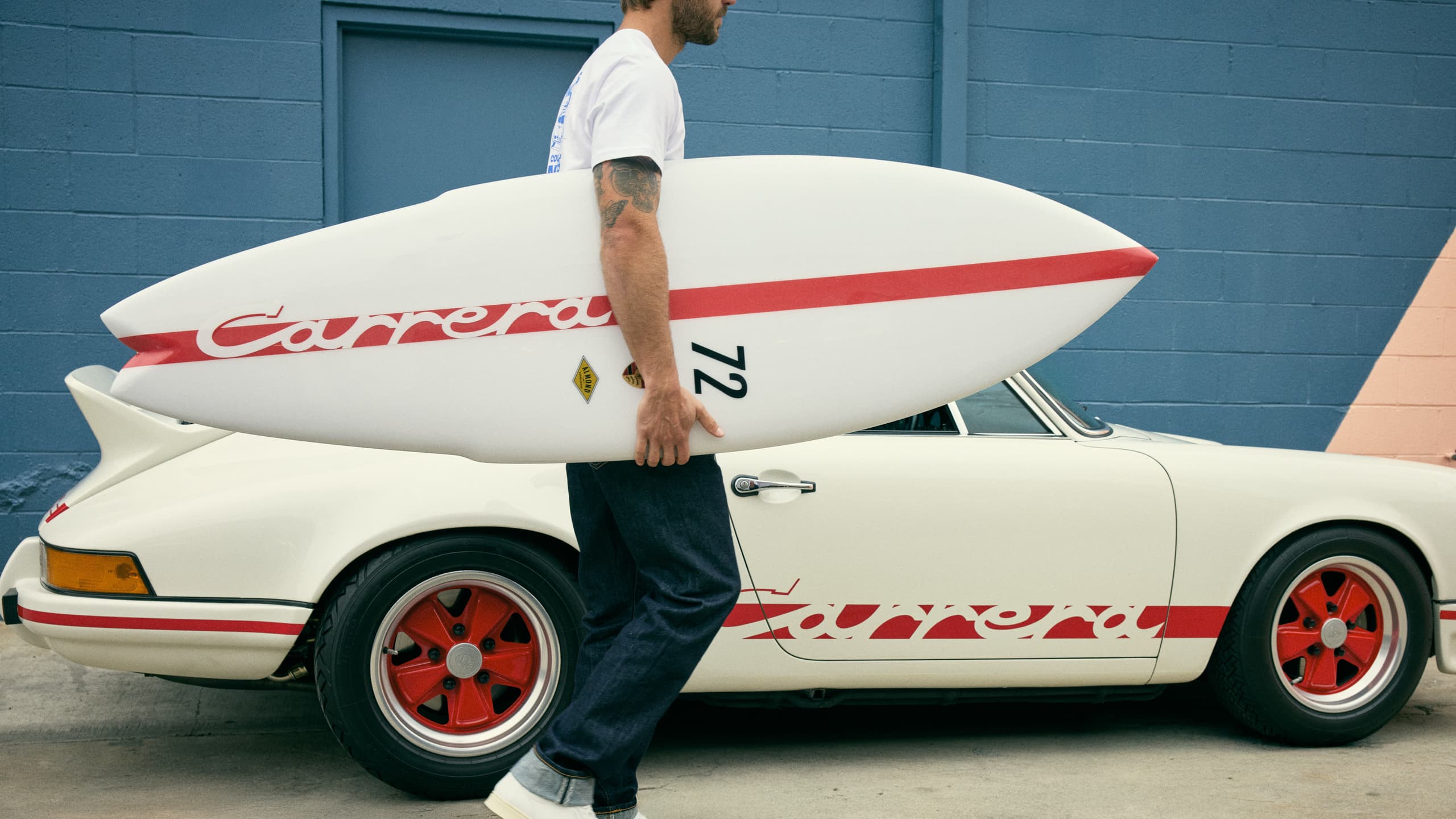 Man walking past Porsche 911 with Porsche Surfboard under his arm