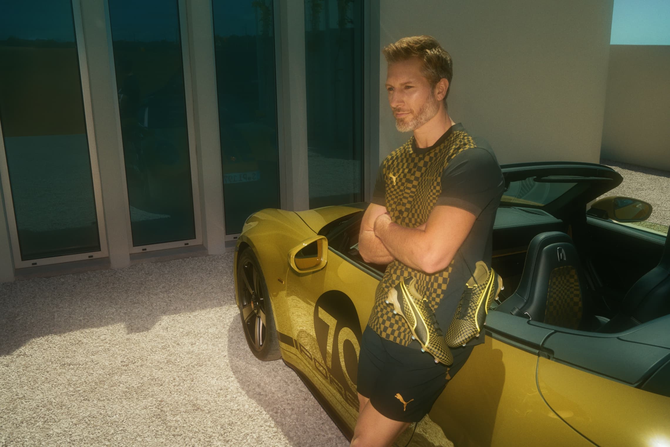 Man wearing sportswear from the 911 Spirit 70 Sport and Football collection and leaning against the Porsche 911 Spirit 70