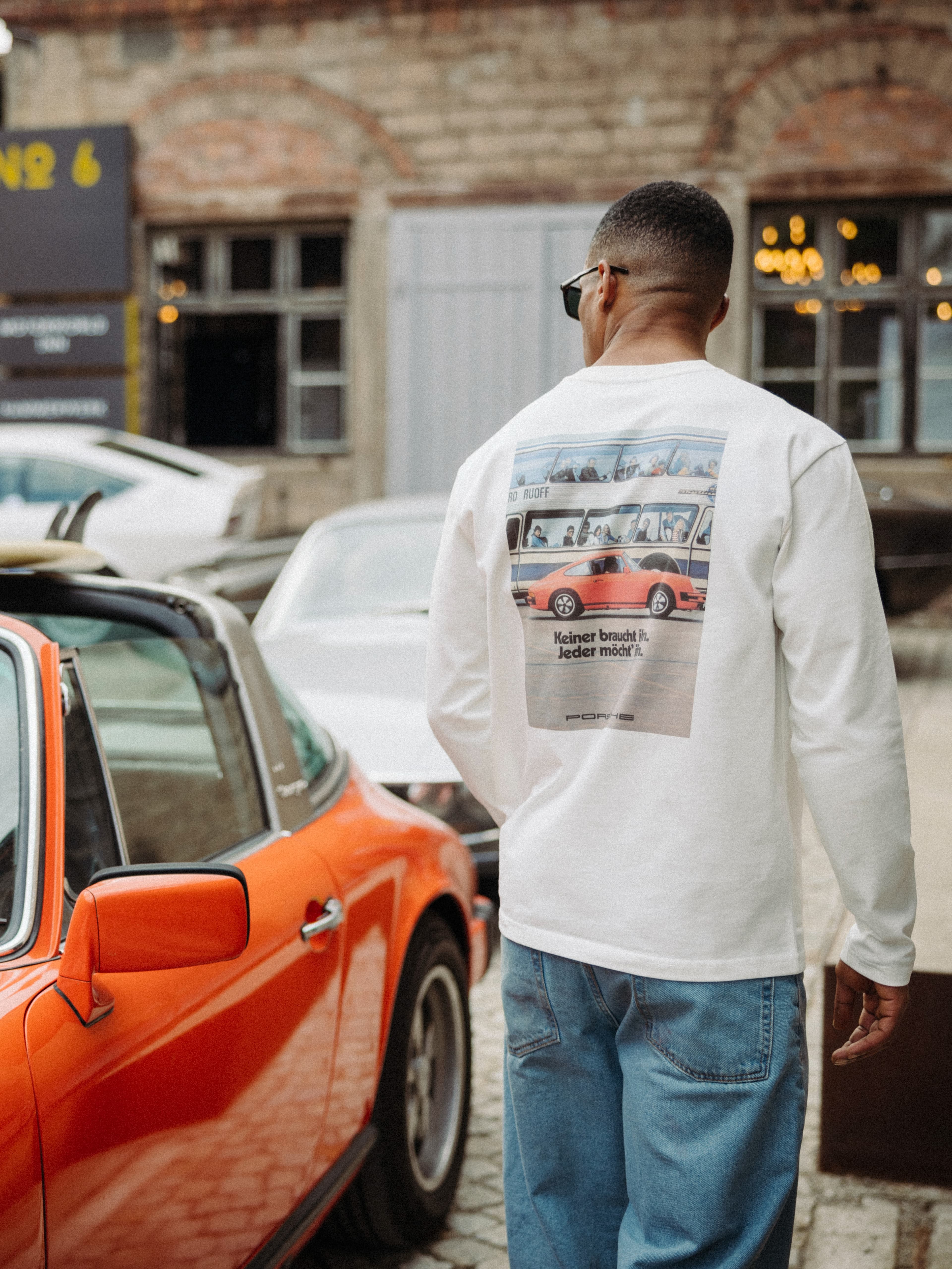Un homme debout à côté d'une Porsche orange, le regard tourné vers l'horizon