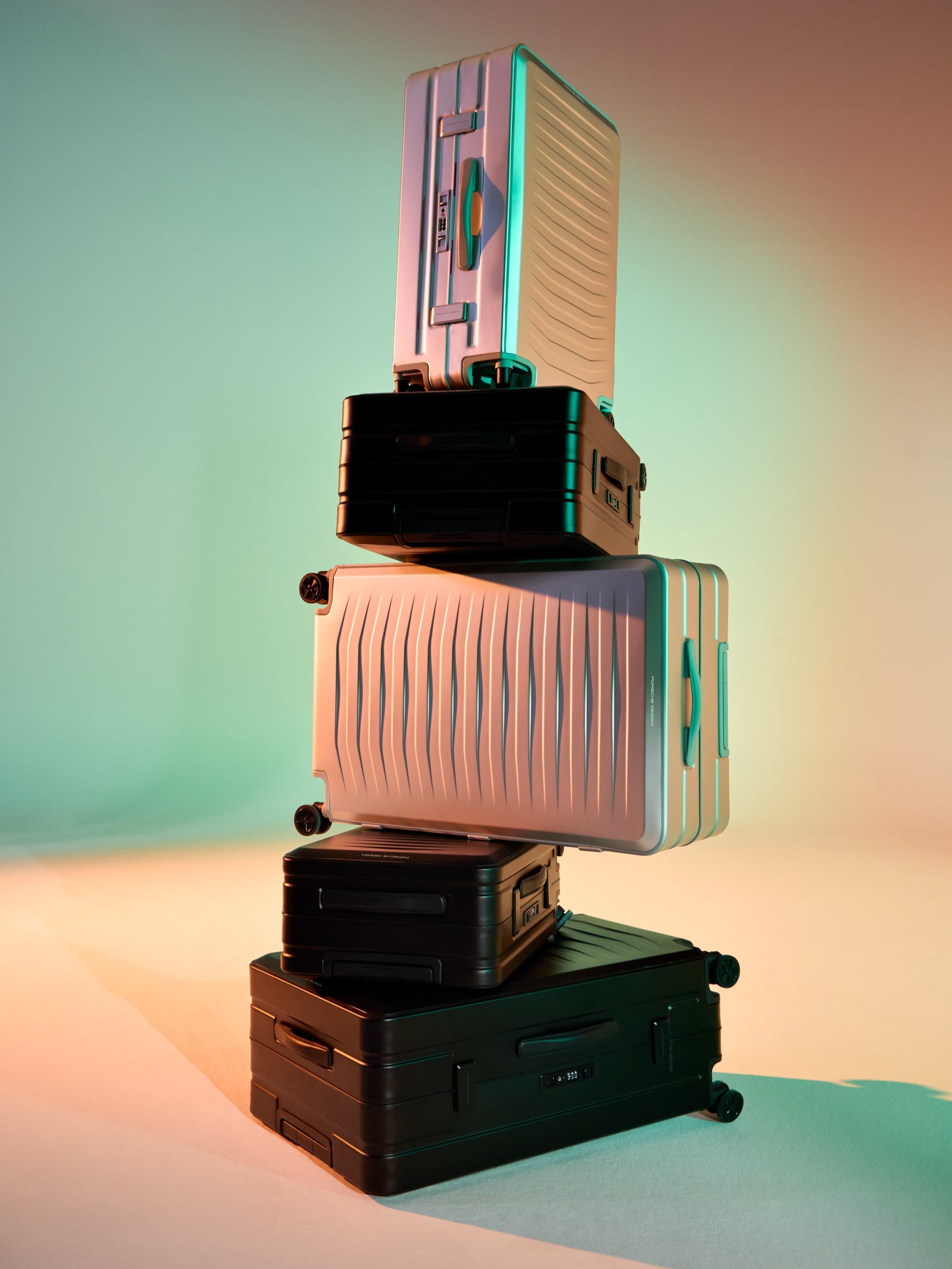 Stacked travel luggage: silver hard-shell suitcase and black suitcases against a pastel-colored background.