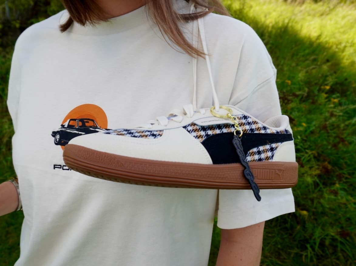 Weiße Sneaker mit Karomuster und brauner Sohle, hängend an einem weißen Shirt mit Porsche-Auto-Grafik, im Freien