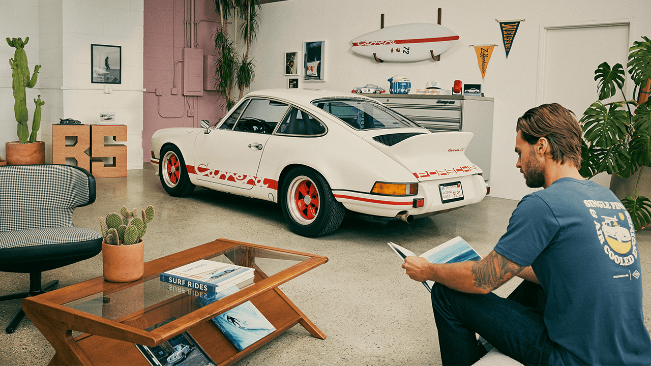 Man sitting in Garage reading a book, Porsche 911 and Porsche Surfboard in background