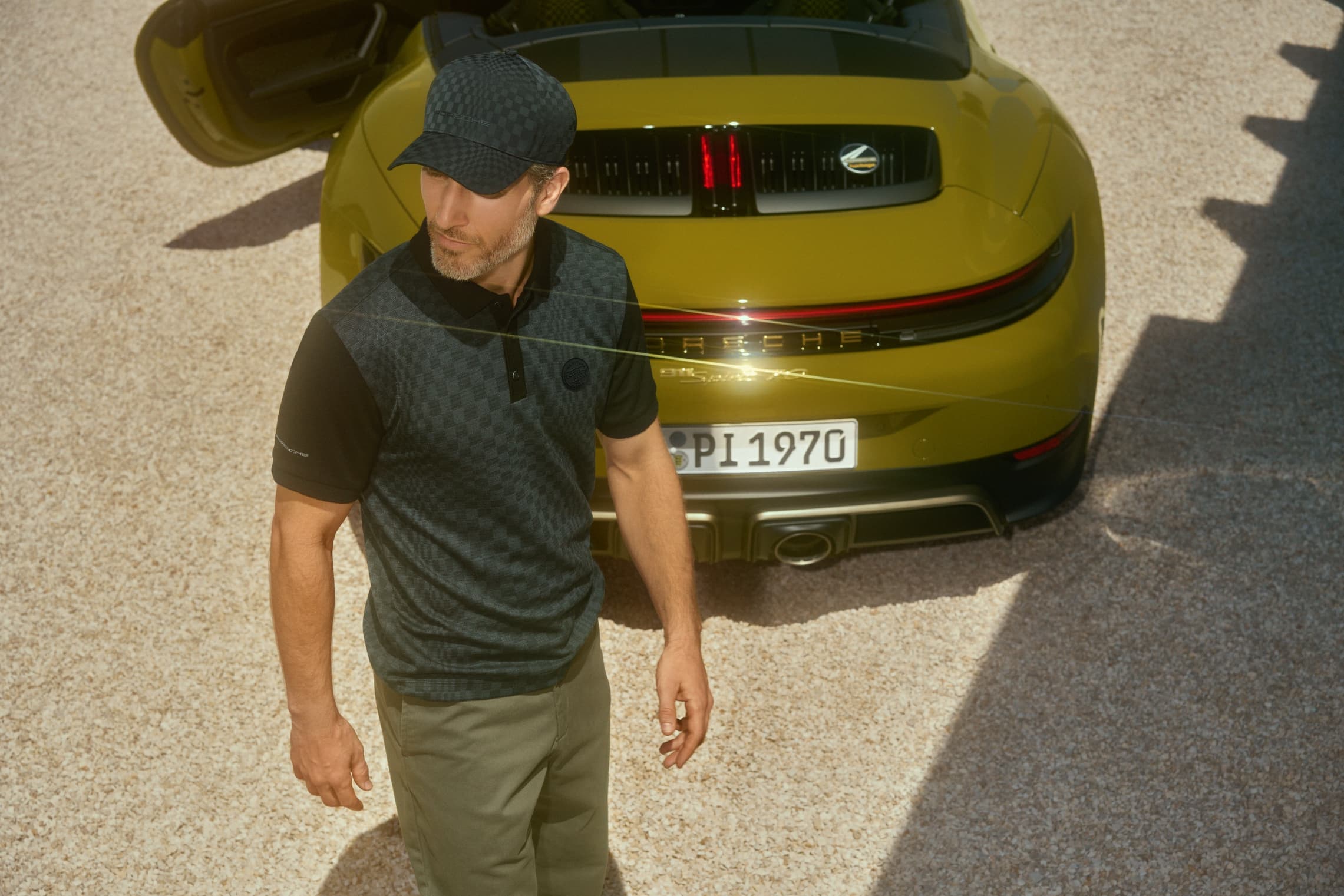 Man wears clothing from the 911 Spirit 70 collection and walks past in front of the Porsche 911 Spirit 70