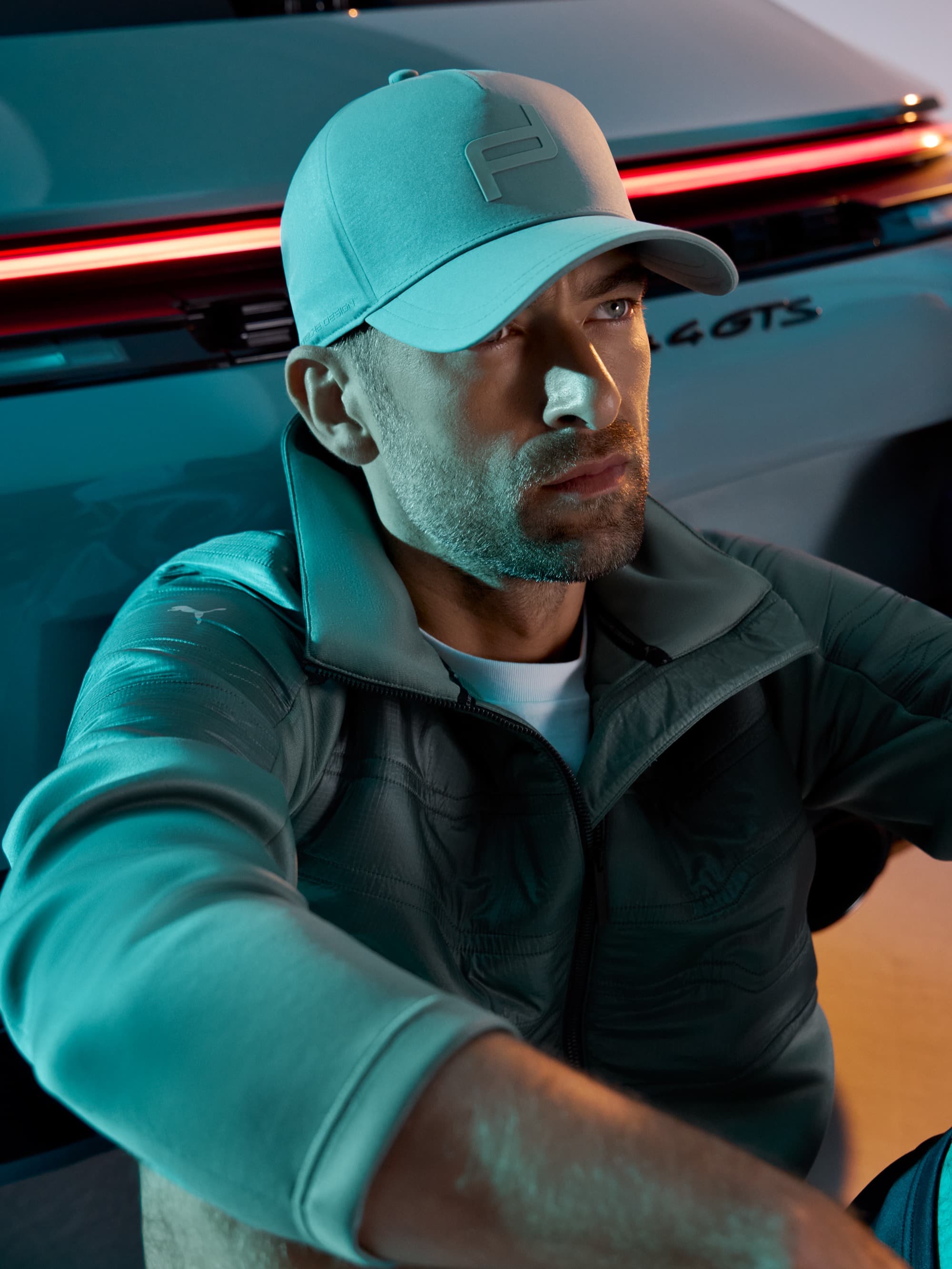 Mann in grauer Mütze und Jacke sitzt nachdenklich neben einem Auto mit roten Rücklichtern