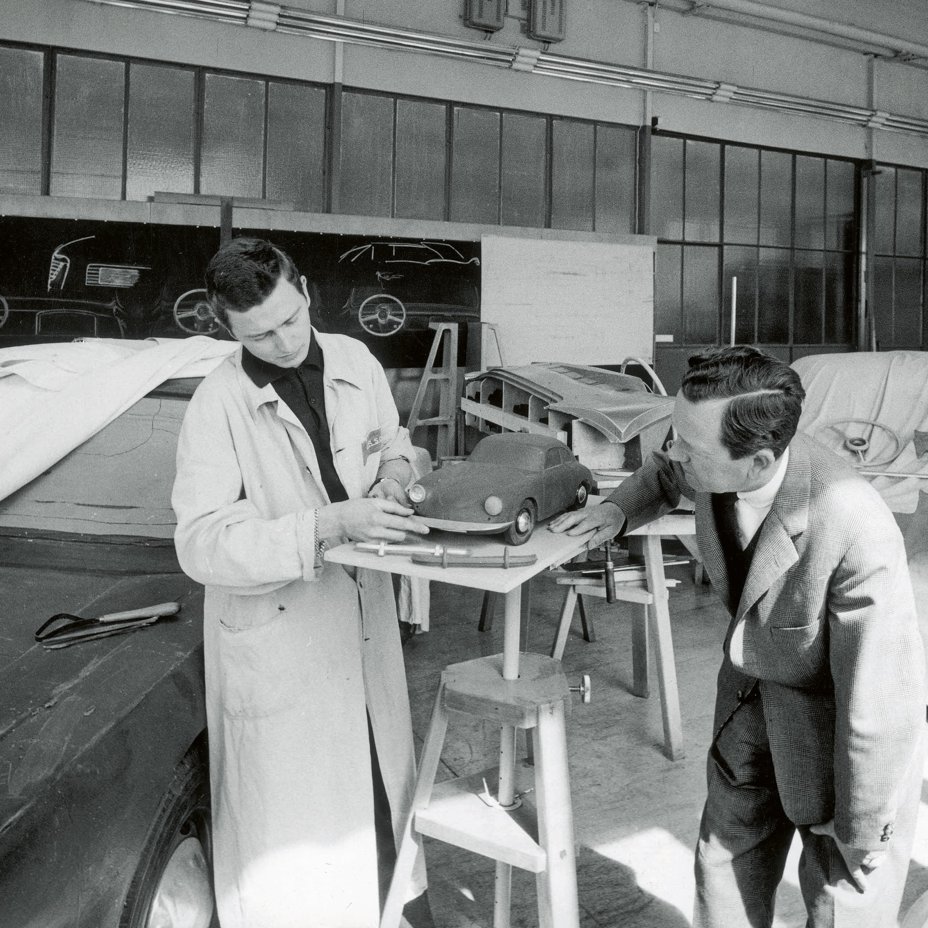 Black-and-white photo: Two designers are examining a model car on a turntable in a workshop.