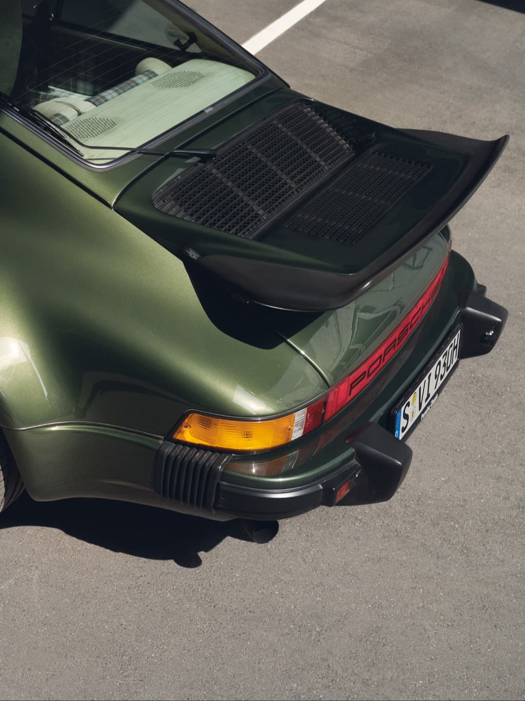 Widok z tyłu oliwkowozielonego Porsche 911 z czarnym tylnym spojlerem i czerwonym pasem świetlnym, na asfalcie.