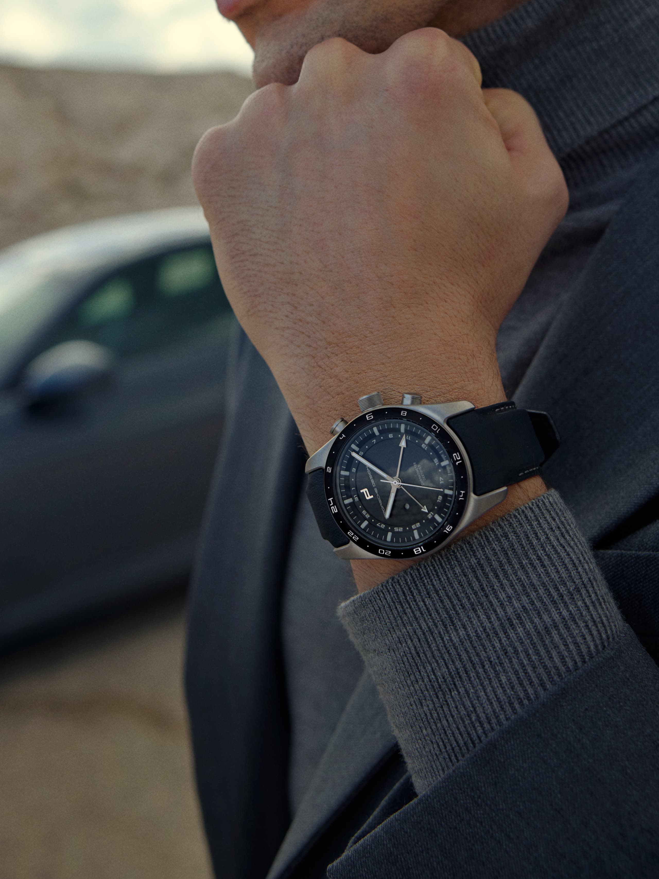mans wrist with Porsche Design Globetimer Chronograph, Porsche 911 blurry in background
