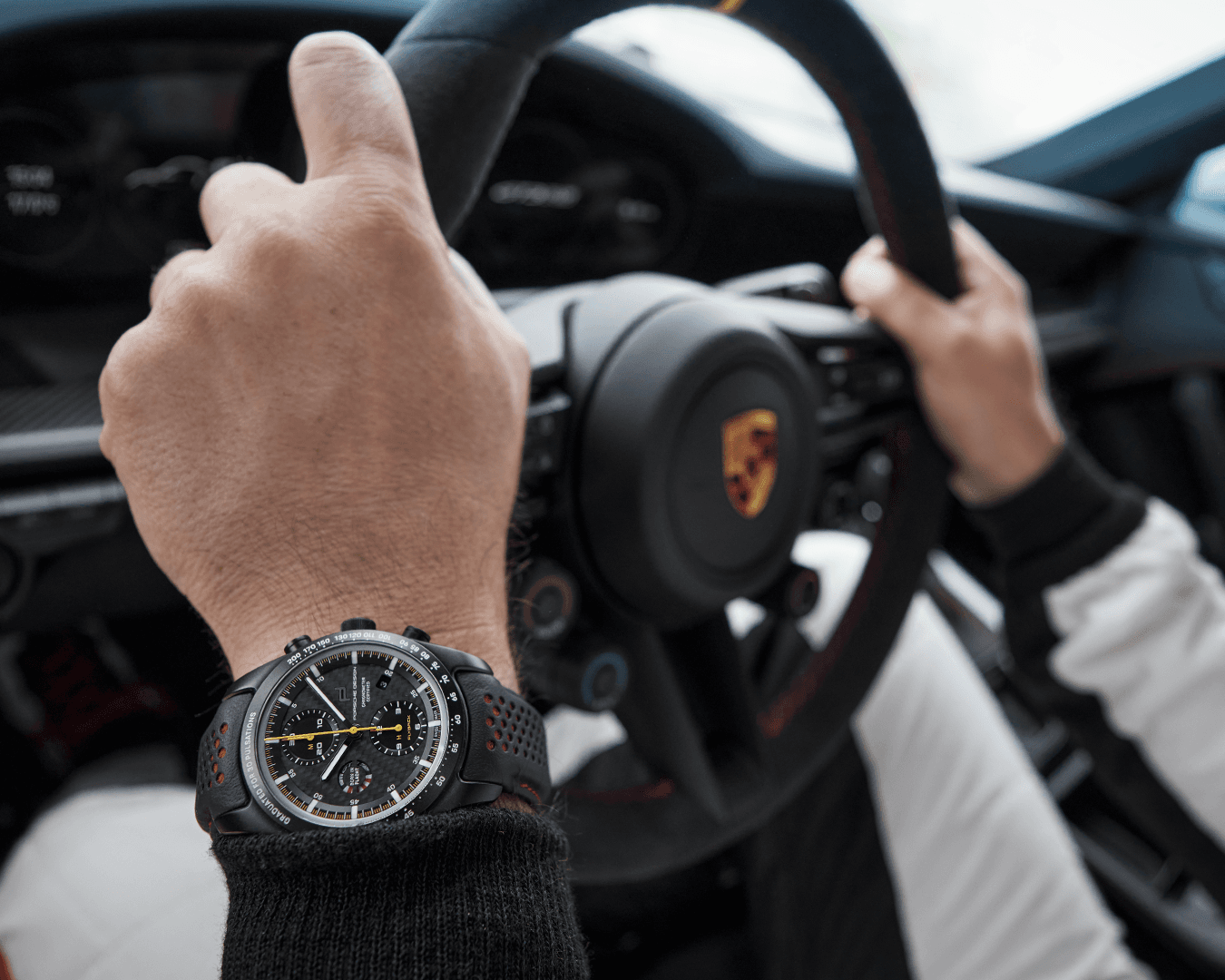 Mężczyzna siedzi w Porsche i trzyma kierownicę. Na nadgarstku ma zegarek Porsche Chronograph 1 GT3 RS.