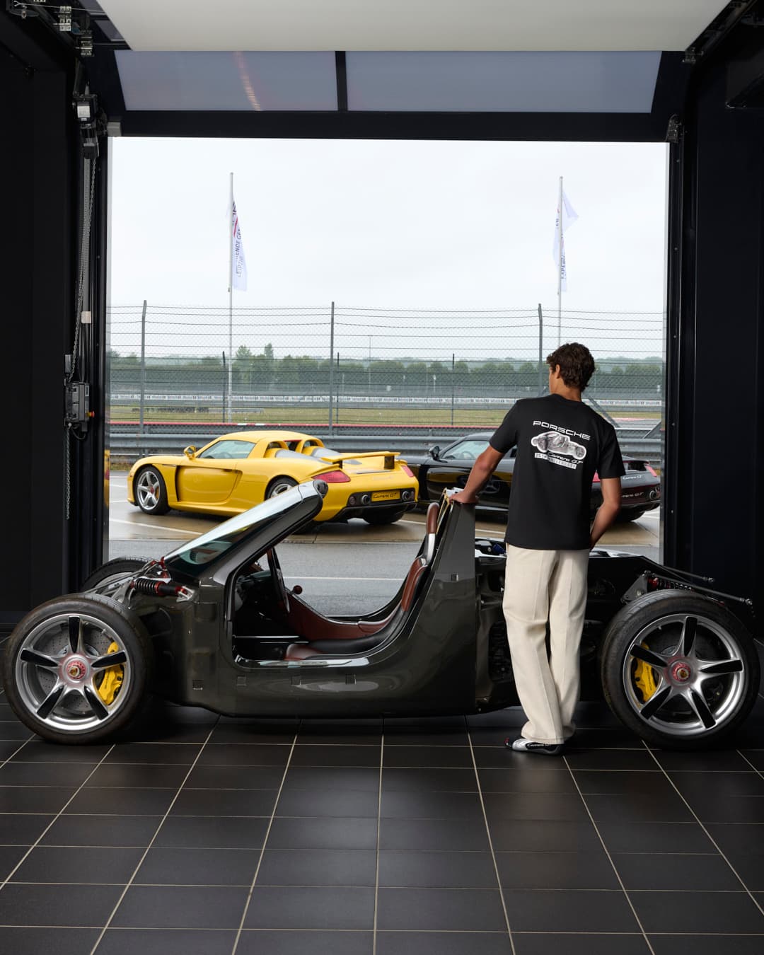 Man wearing a T-shirt from the Porsche Carrera GT 25th Anniversary Collection standing in front of a chassis