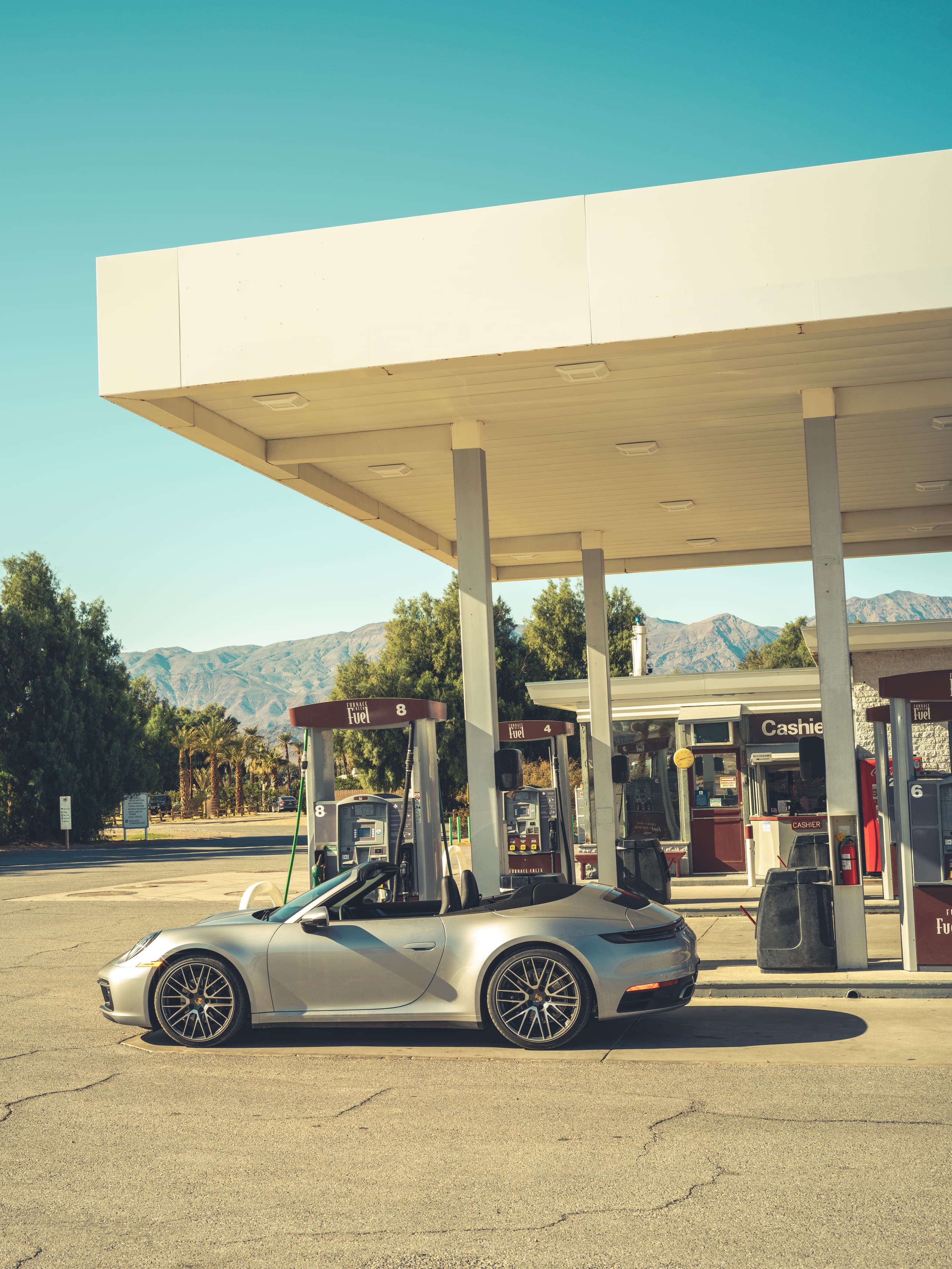 A silver Porsche 911 photgraphing from the side stops at a gas station
