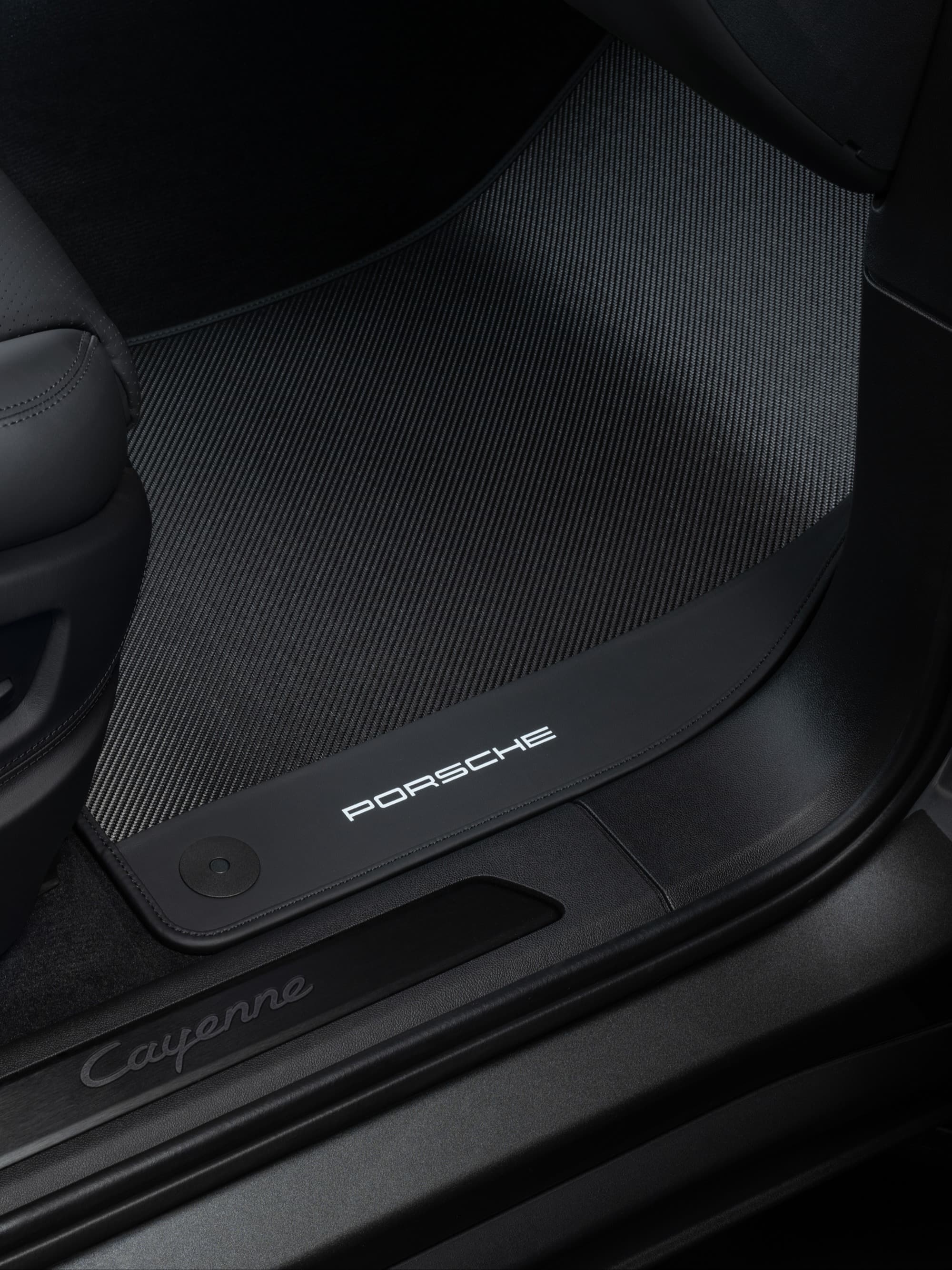 Black Porsche Cayenne floor mat with logo, textured surface, and sleek design in car interior.