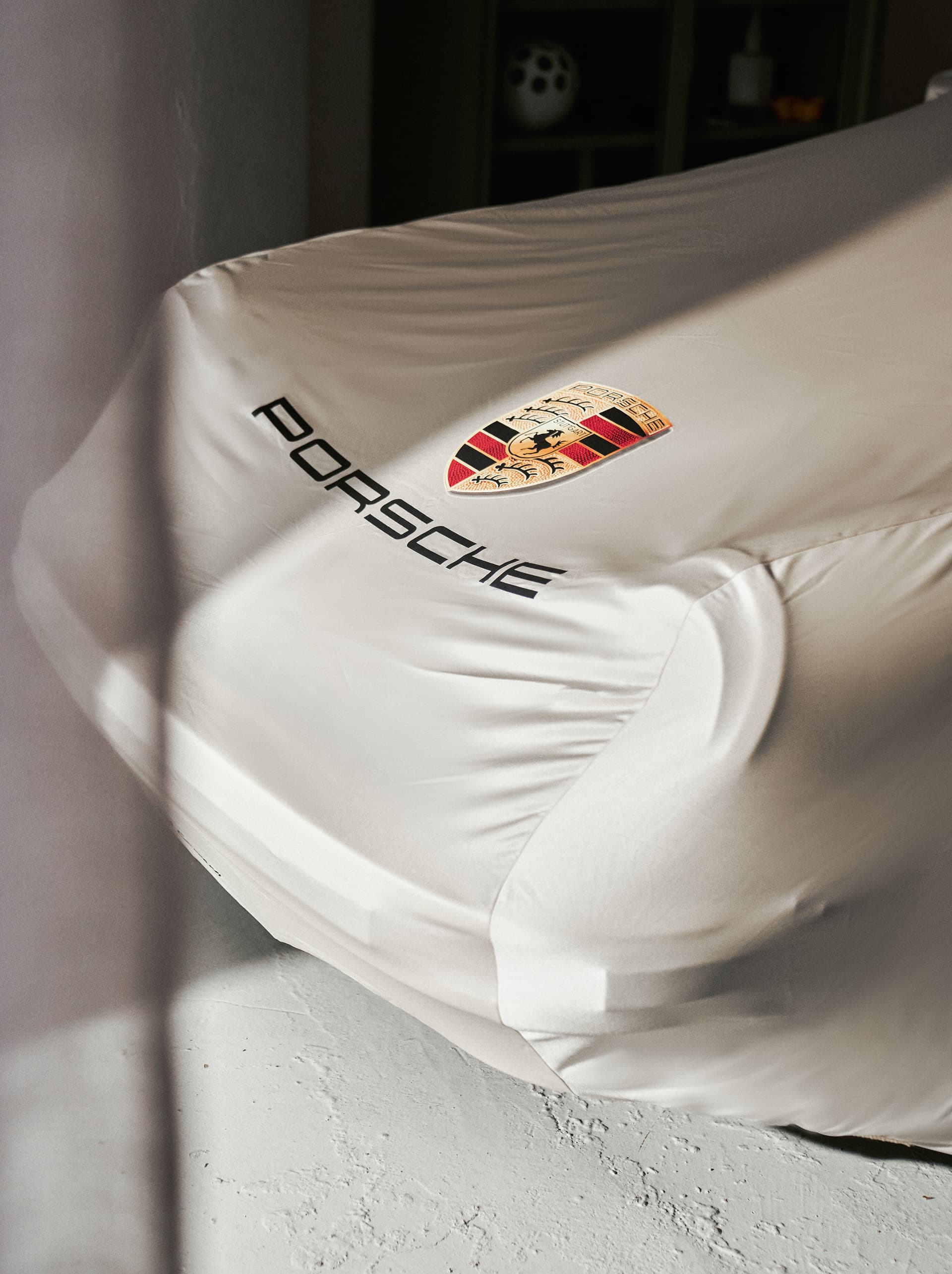 Auto mit einer beigen Porsche-Abdeckung, mit Porsche-Logo, auf hellem Boden