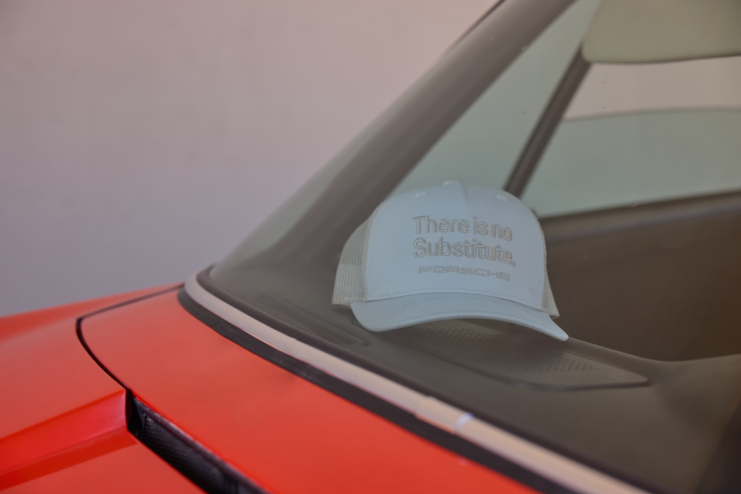 White and tan Porsche trucker cap with “There is no Substitute.” embroidery on the dashboard of a red car.