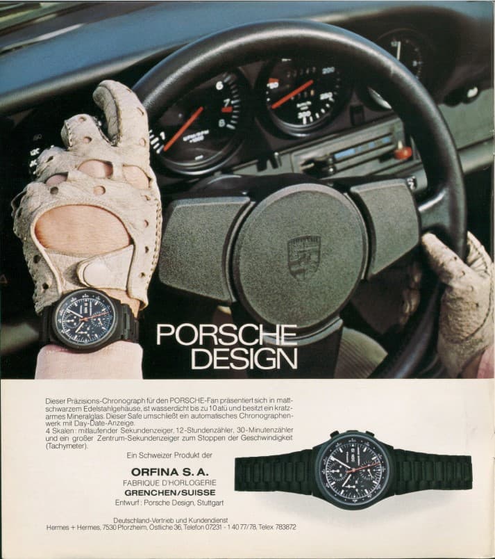 Driving gloves on the Porsche steering wheel, focus on a black Porsche Design chronograph watch on the wrist.