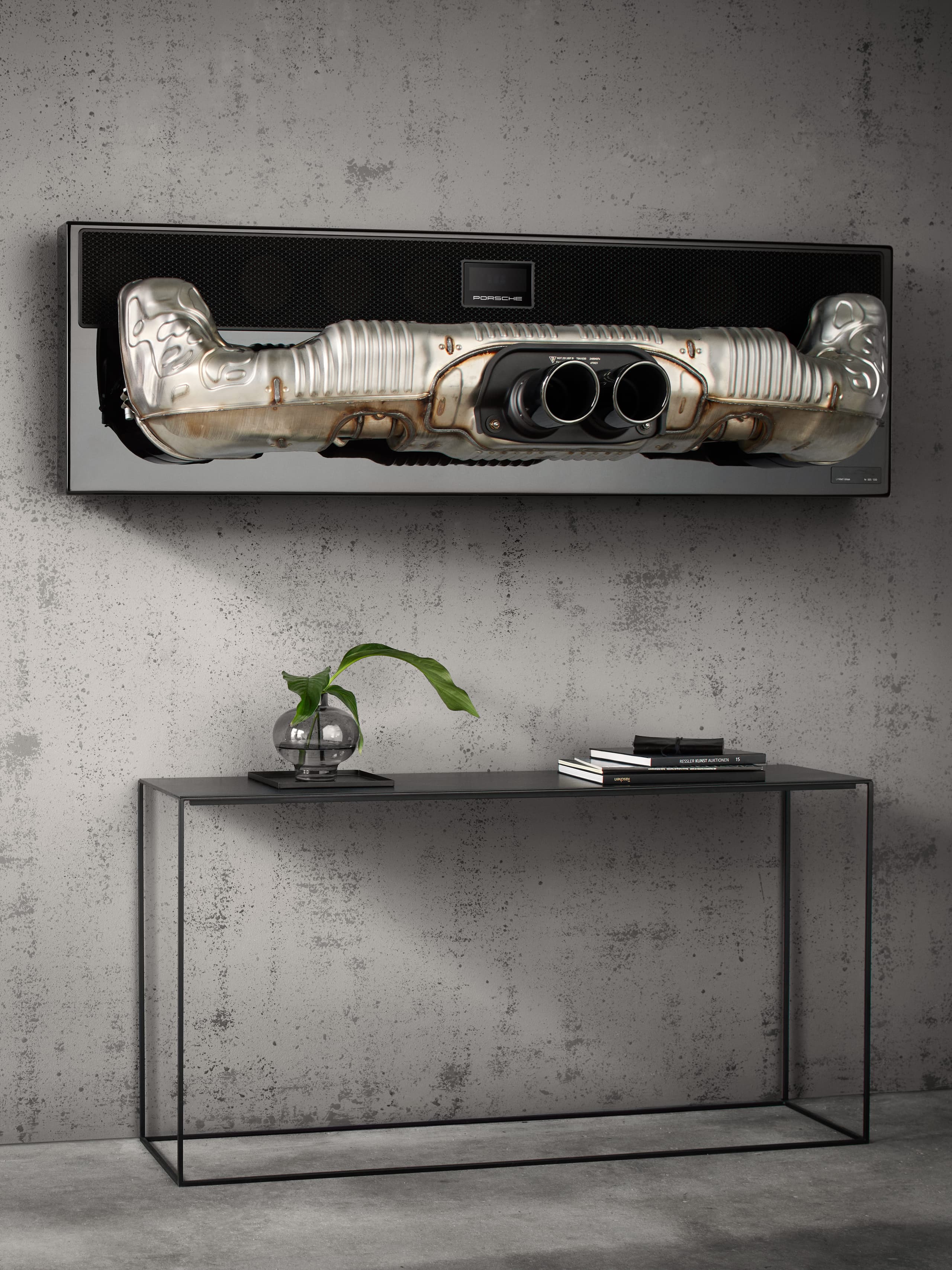 You can see the Porsche soundbar hanging on a grey stone wall. Below there is a black sideboard.