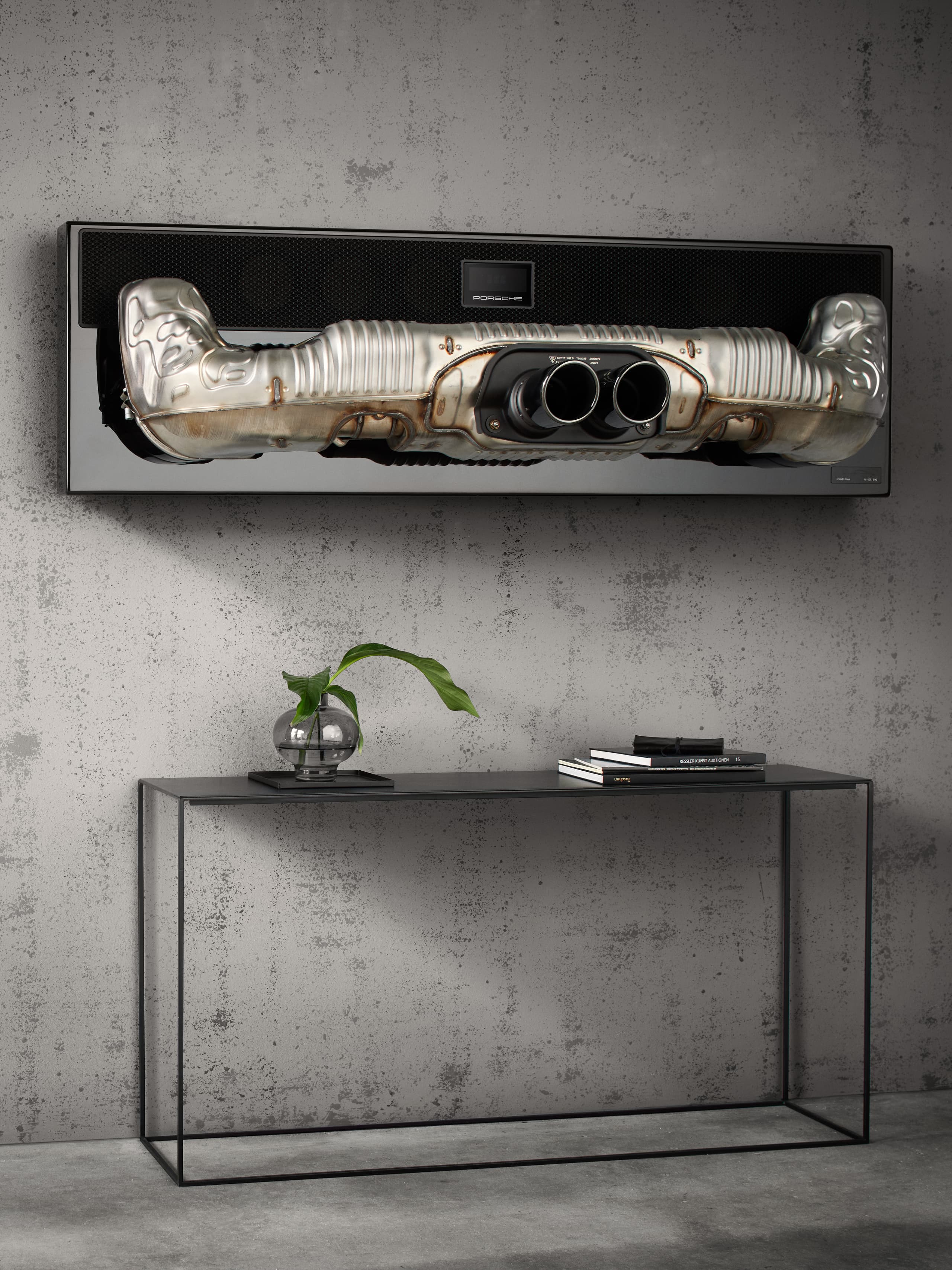 You can see the Porsche soundbar hanging on a grey stone wall. Below there is a black sideboard.