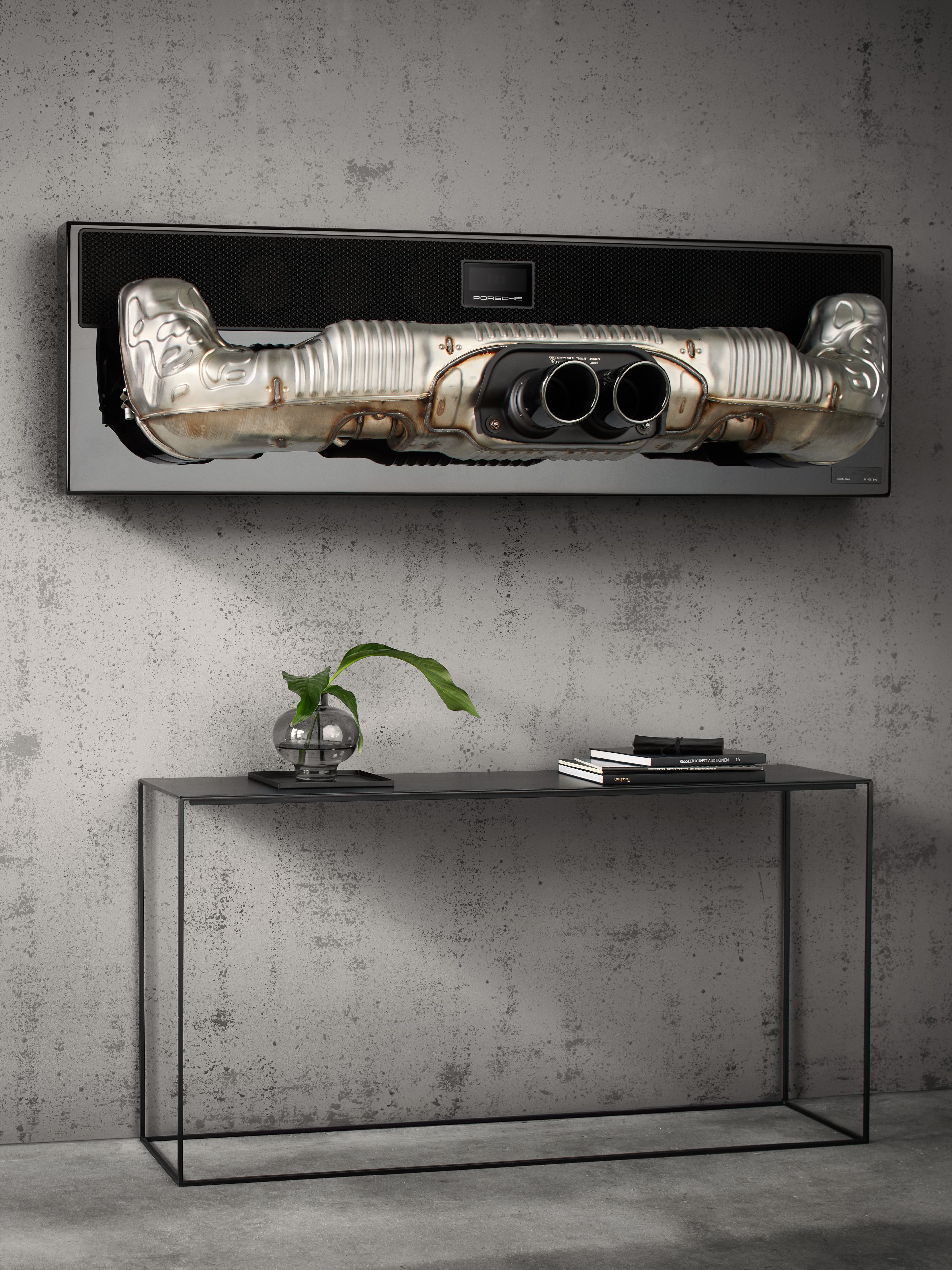 Porsche soundbar hanging on a grey stone wall. Below there is a black sideboard.