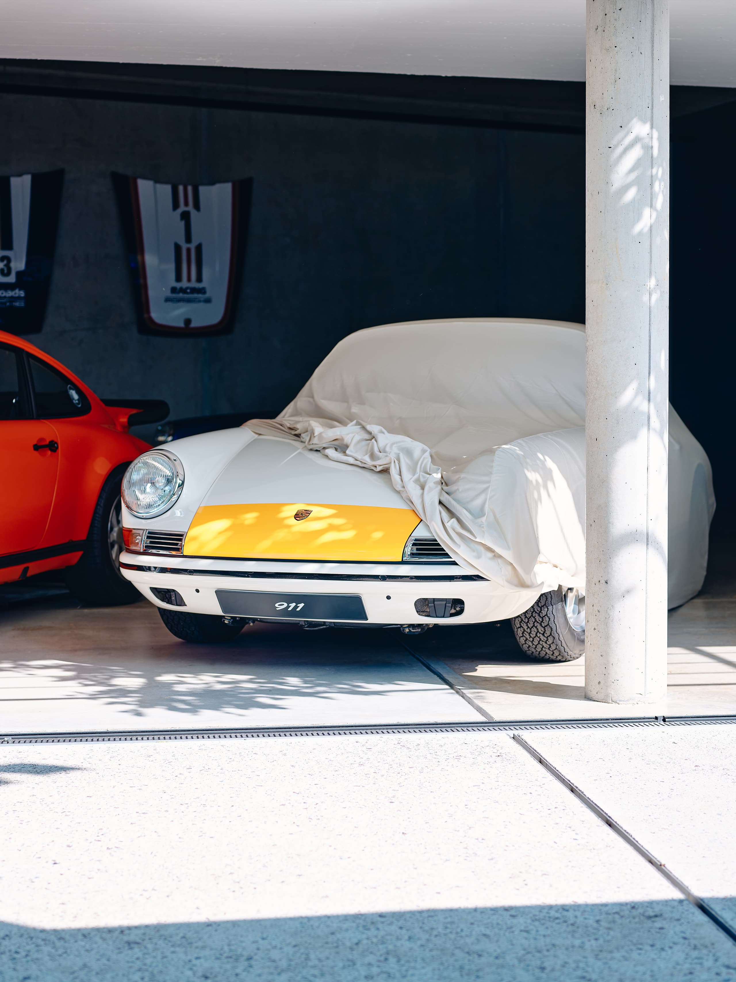 You can see a white and yellow historic Porsche 911 beneath a beige car cover