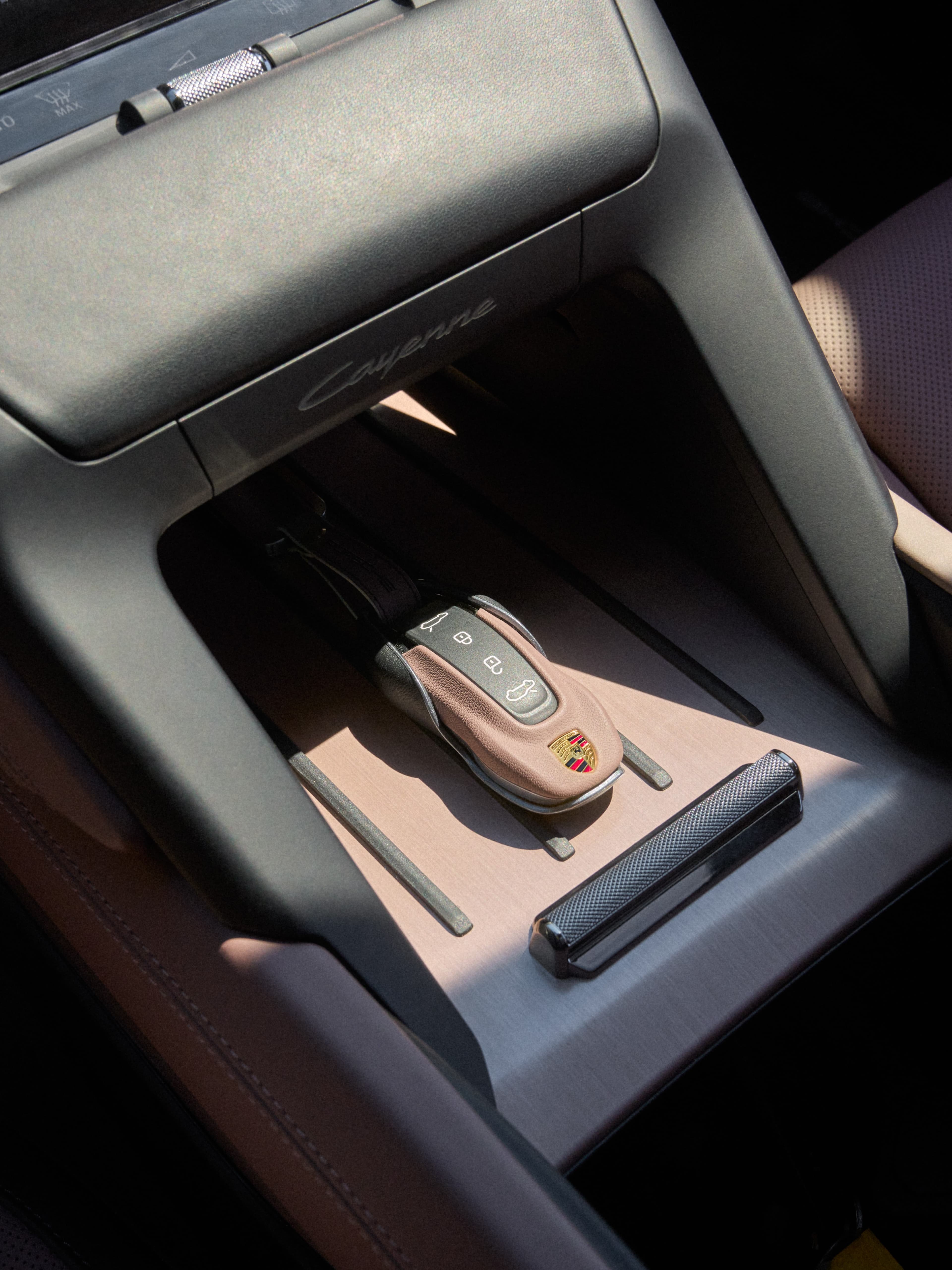 Close-up of Porsche center console with brown leather key fob on brushed metal tray and black trim.