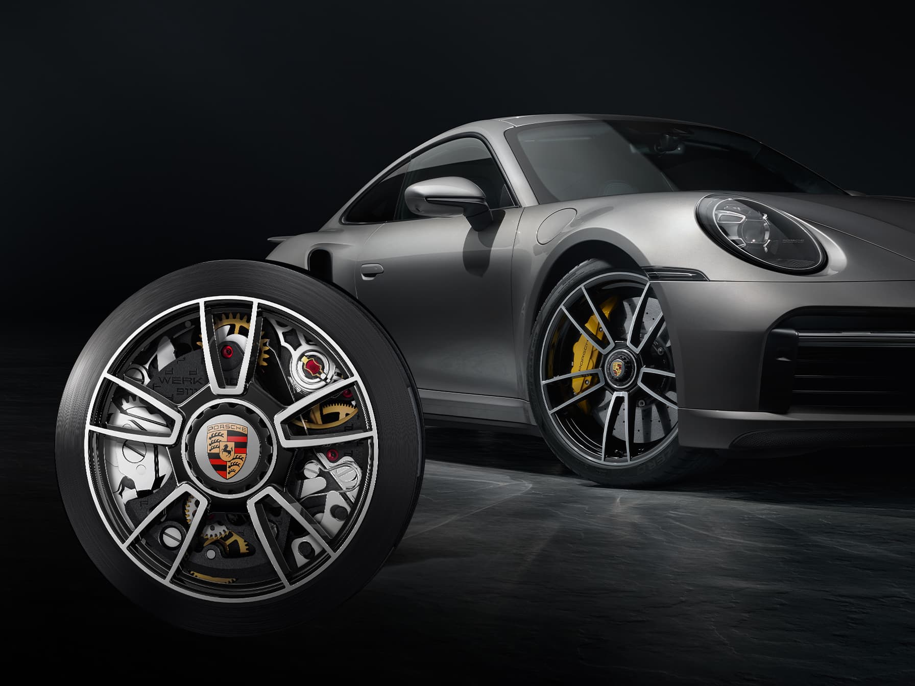 Silberner Porsche 911 mit Nahaufnahme einer Felge im Vordergrund, schwarzer Hintergrund.